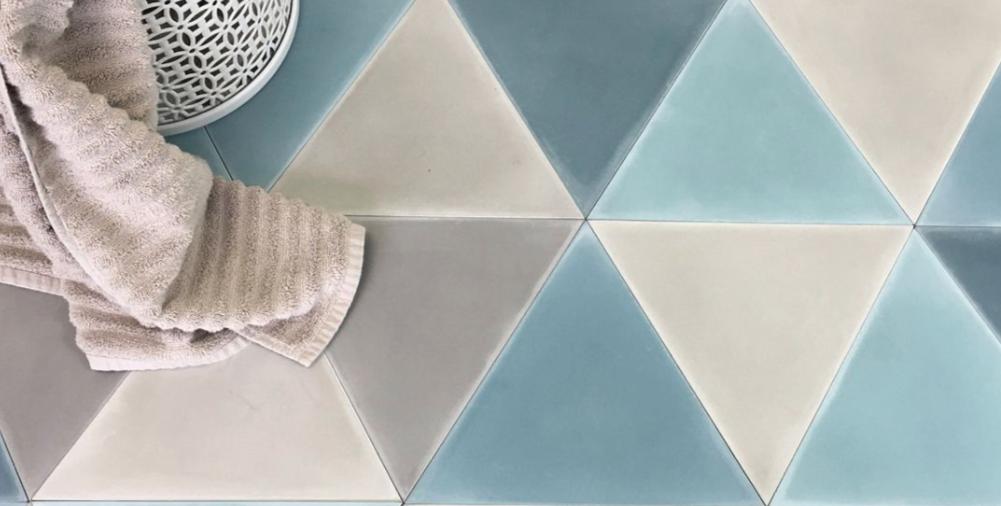Geometric floor tiles in shades of blue, gray, and white forming a pattern of triangles, with a beige towel and a white basket placed on top.