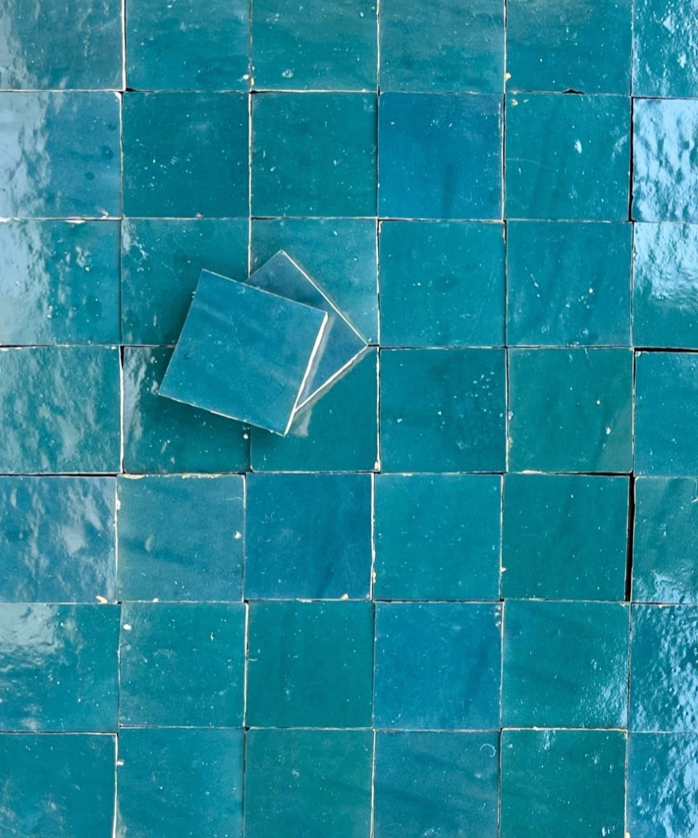 Several glossy, square blue-green tiles are arranged in a grid, with three loose tiles placed on top at an angle, creating a layered effect.