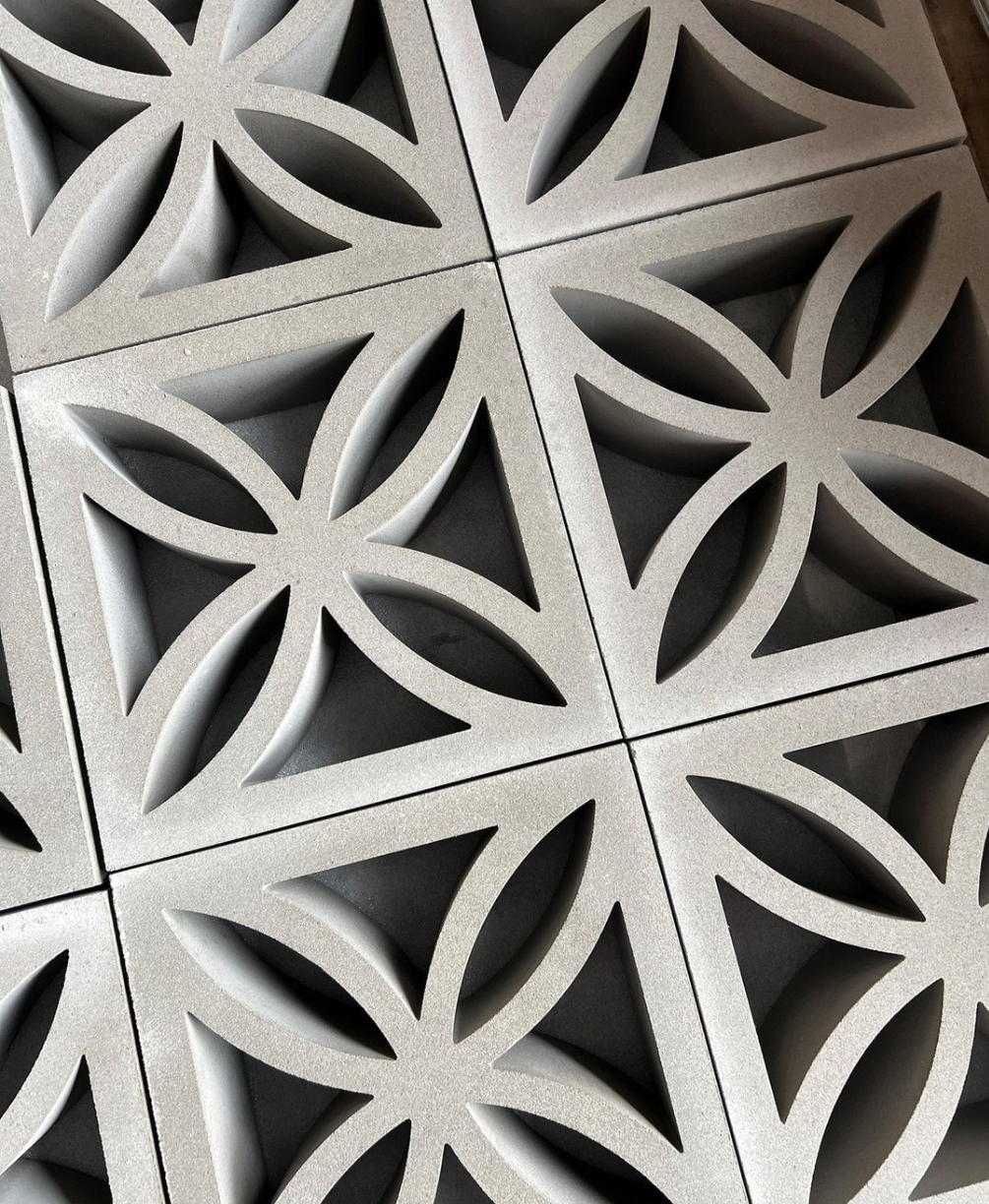 Close-up of decorative concrete blocks with a geometric floral pattern, forming repeating overlapping petal shapes. The blocks are light gray and arranged in a neat, interlocking grid.