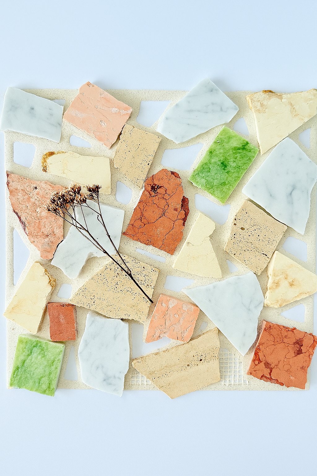 Candy - Puzzle stone sample by New York Cement Tile displayed on white, accented with a small dried flower.