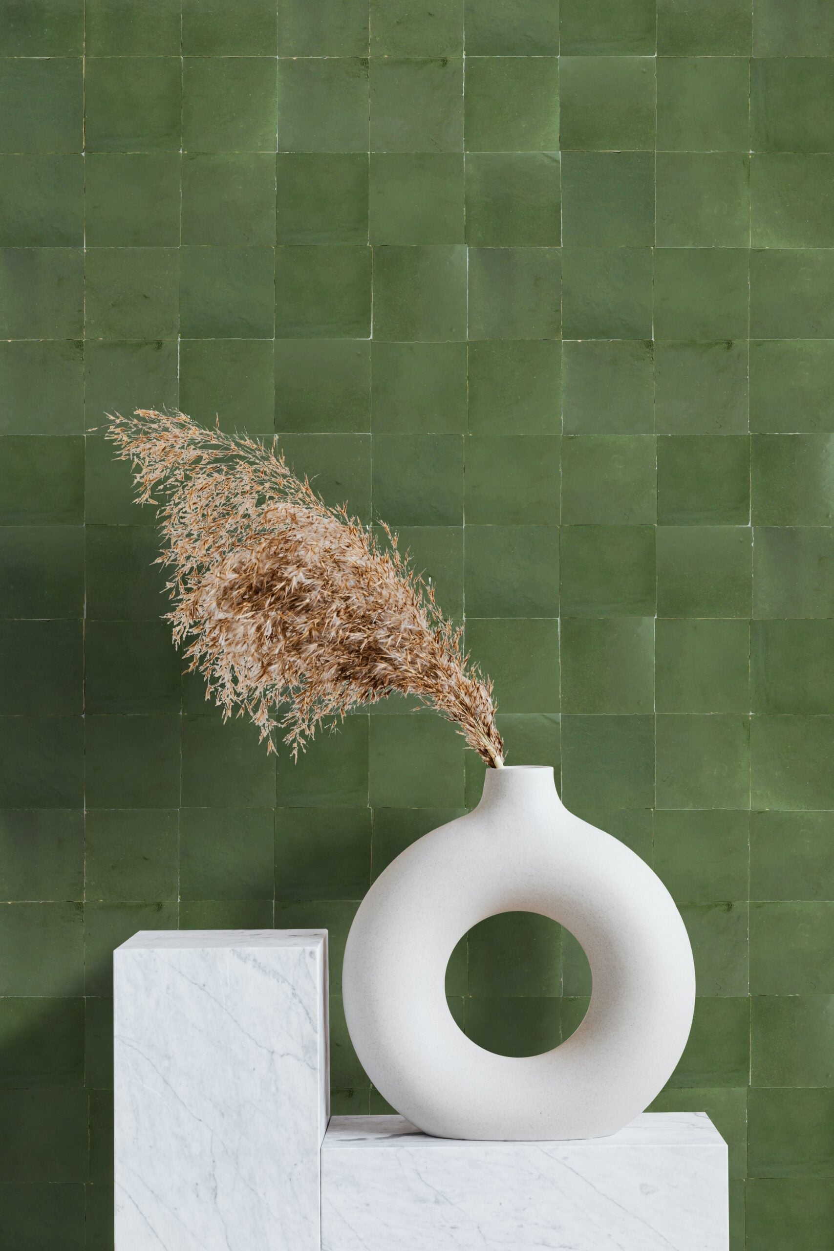 A round white vase with dried grass on marble pedestals, set against Moss Green tiles by New York Cement Tile.