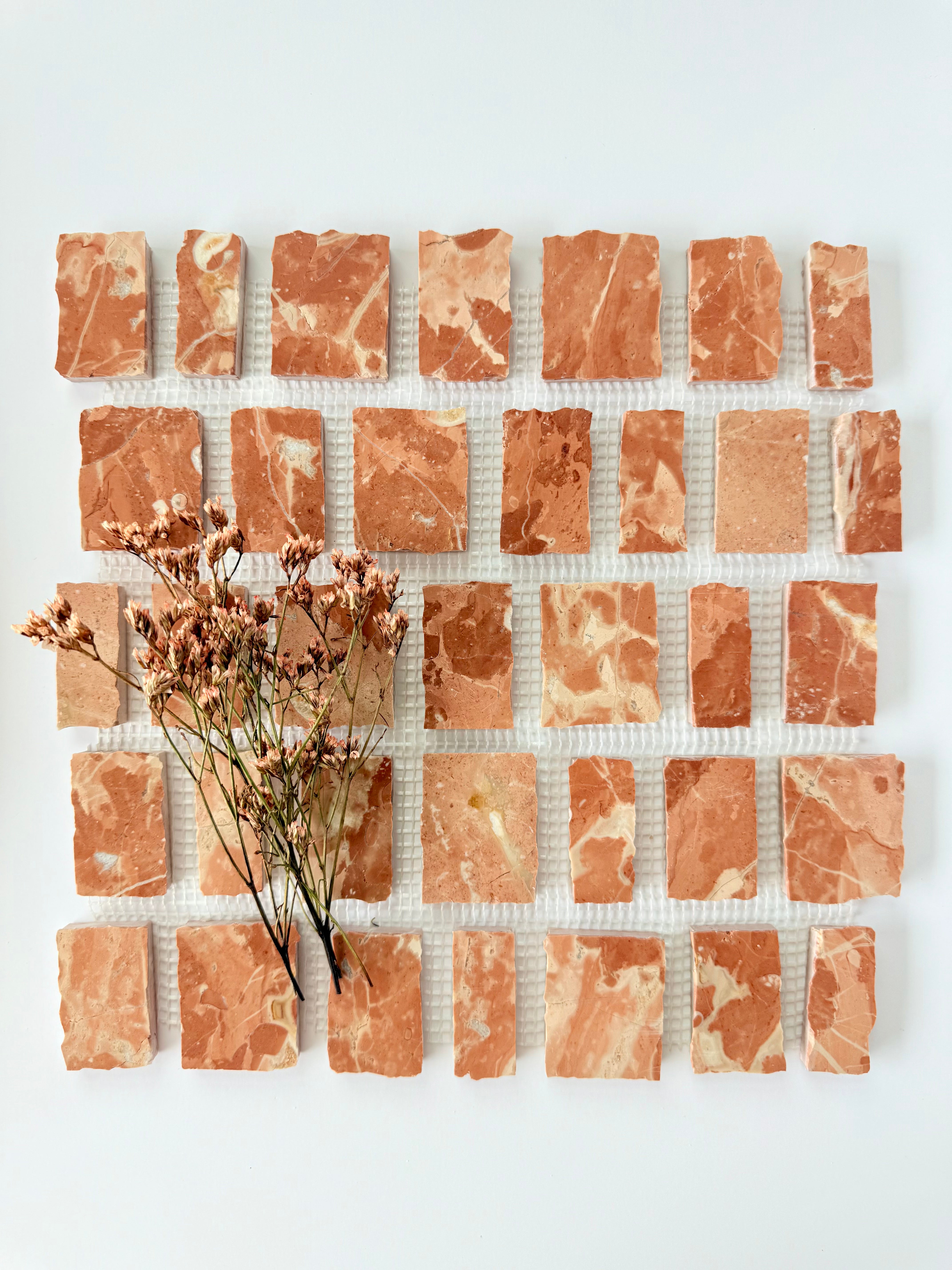 Scarpa I Earth Mosaic Marble Mesh tiles by New York Cement Tile, styled with dried flowers on a white background.