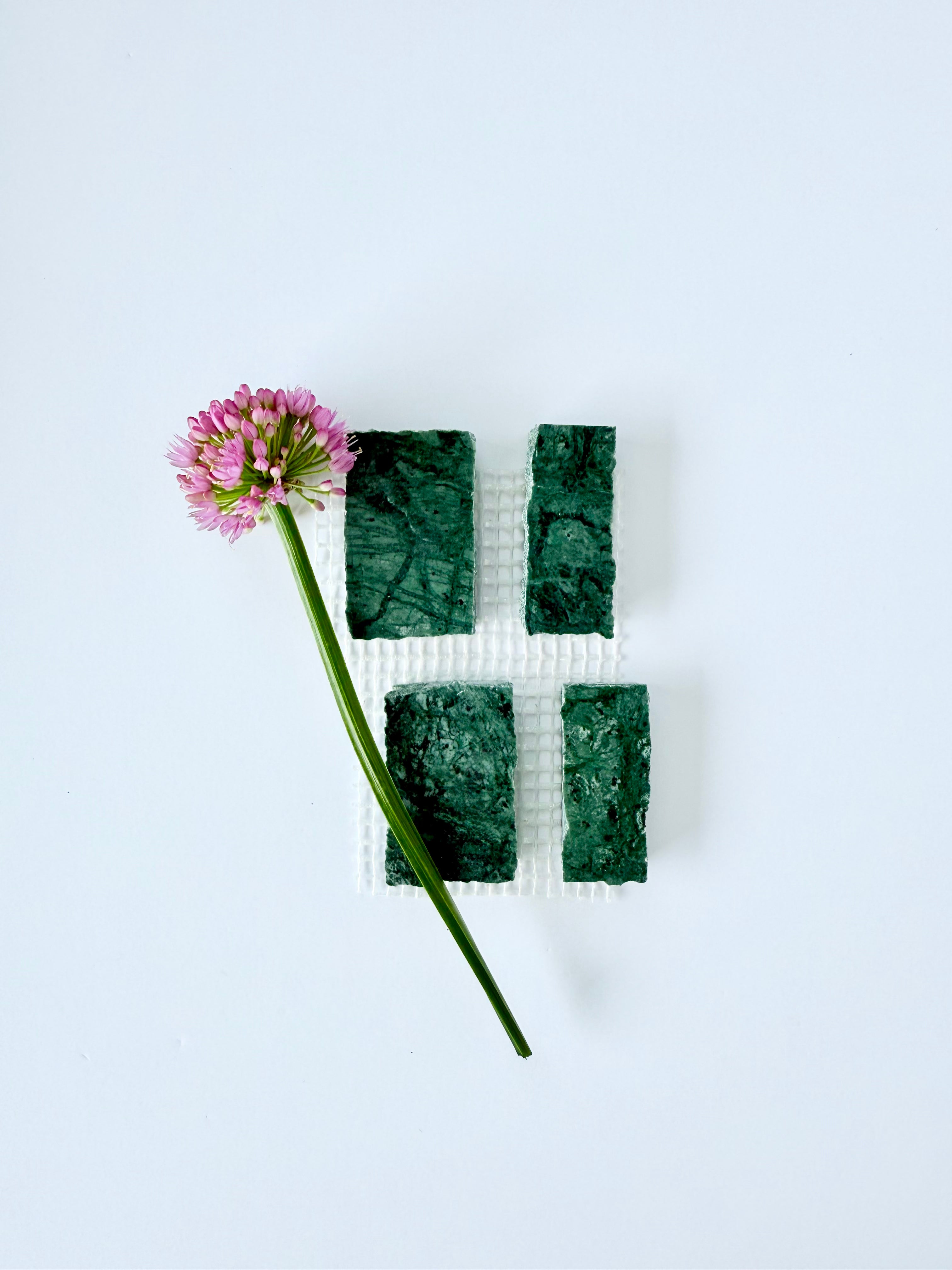 A pink flower on white beside four Scarpa I Emerald Mosaic Marble Mesh tiles by New York Cement Tile in a grid.