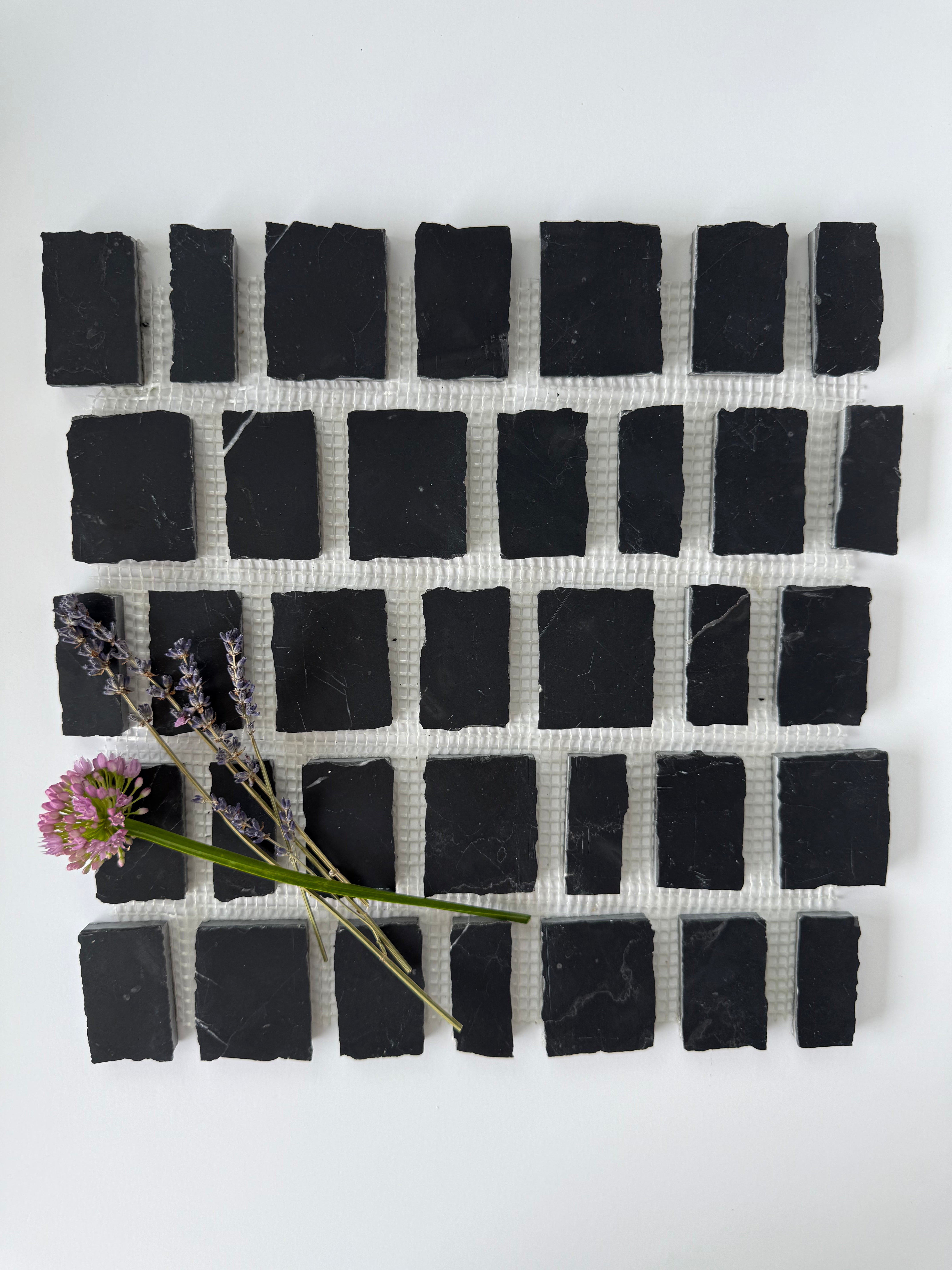 Scarpa I Black Rough Marble Mesh by New York Cement Tile, sample shown with lavender sprig and pink flower on top.