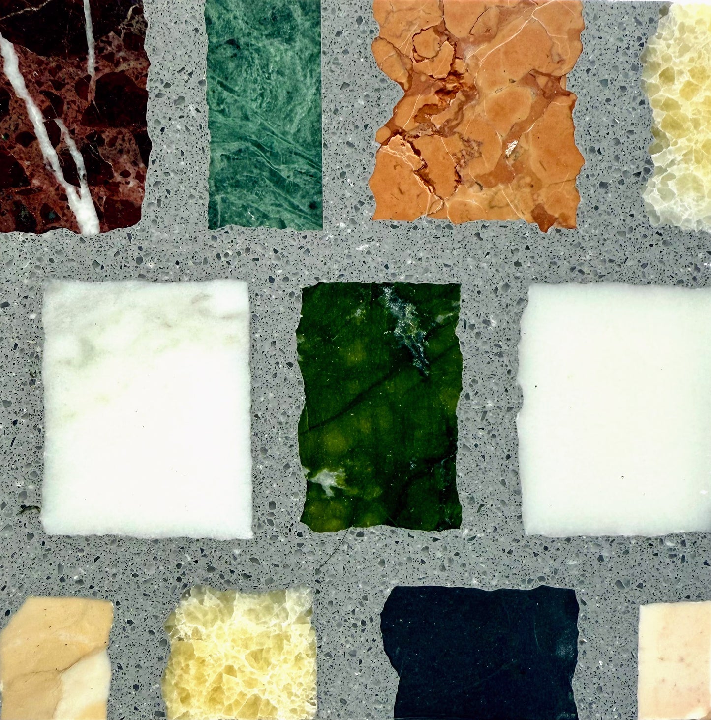 Carlo Scarpa- Multicolor Dark by New York Cement Tile: a grid of colorful, textured marble and stone tiles in gray concrete.
