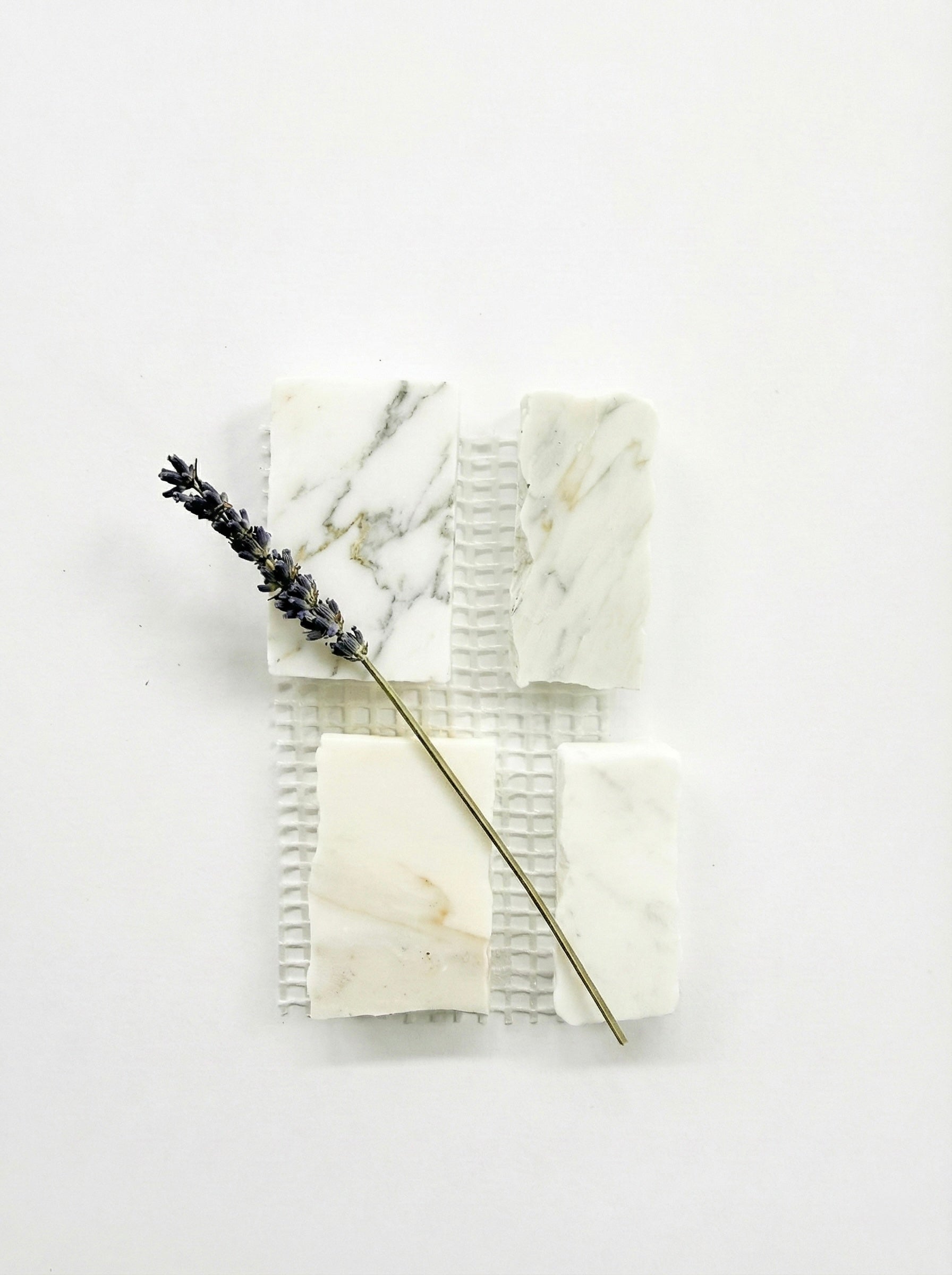 Four Scarpa I Calacatta Gold Marble Mesh samples by New York Cement Tile and a sprig of lavender on a white background.