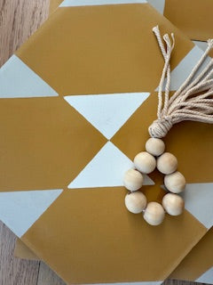 NL20-4D hexagonal mustard-yellow tile by New York Cement Tile, with white triangles and a beaded tassel keychain on top.