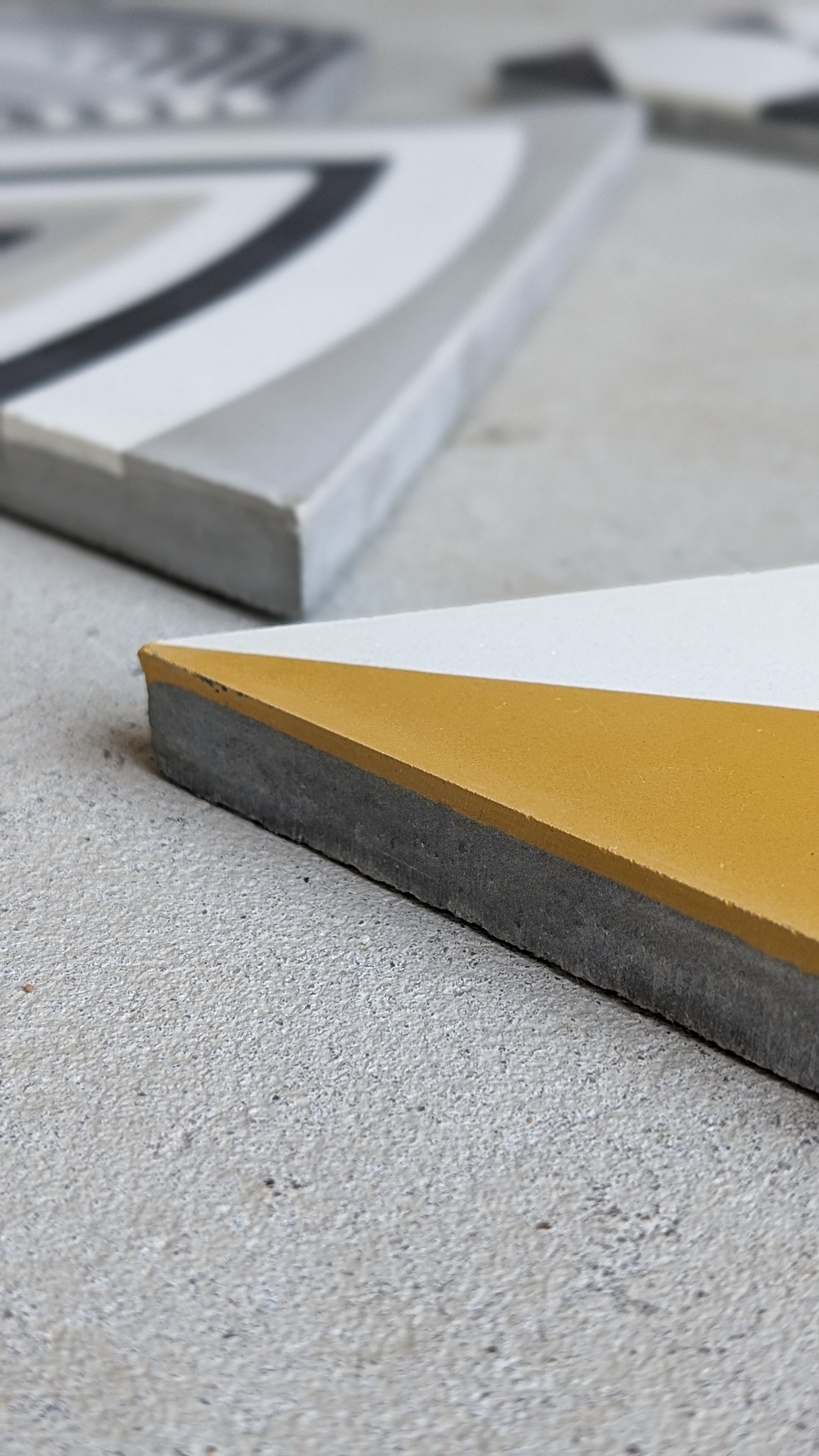 A close-up of geometric ceramic tiles on a concrete surface, featuring white, gray, and yellow sections.