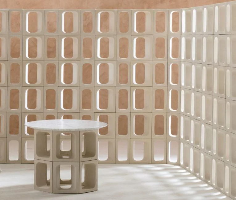 A round GLAPA table by New York Cement Tile stands in a corner of light block walls with oval cutouts.