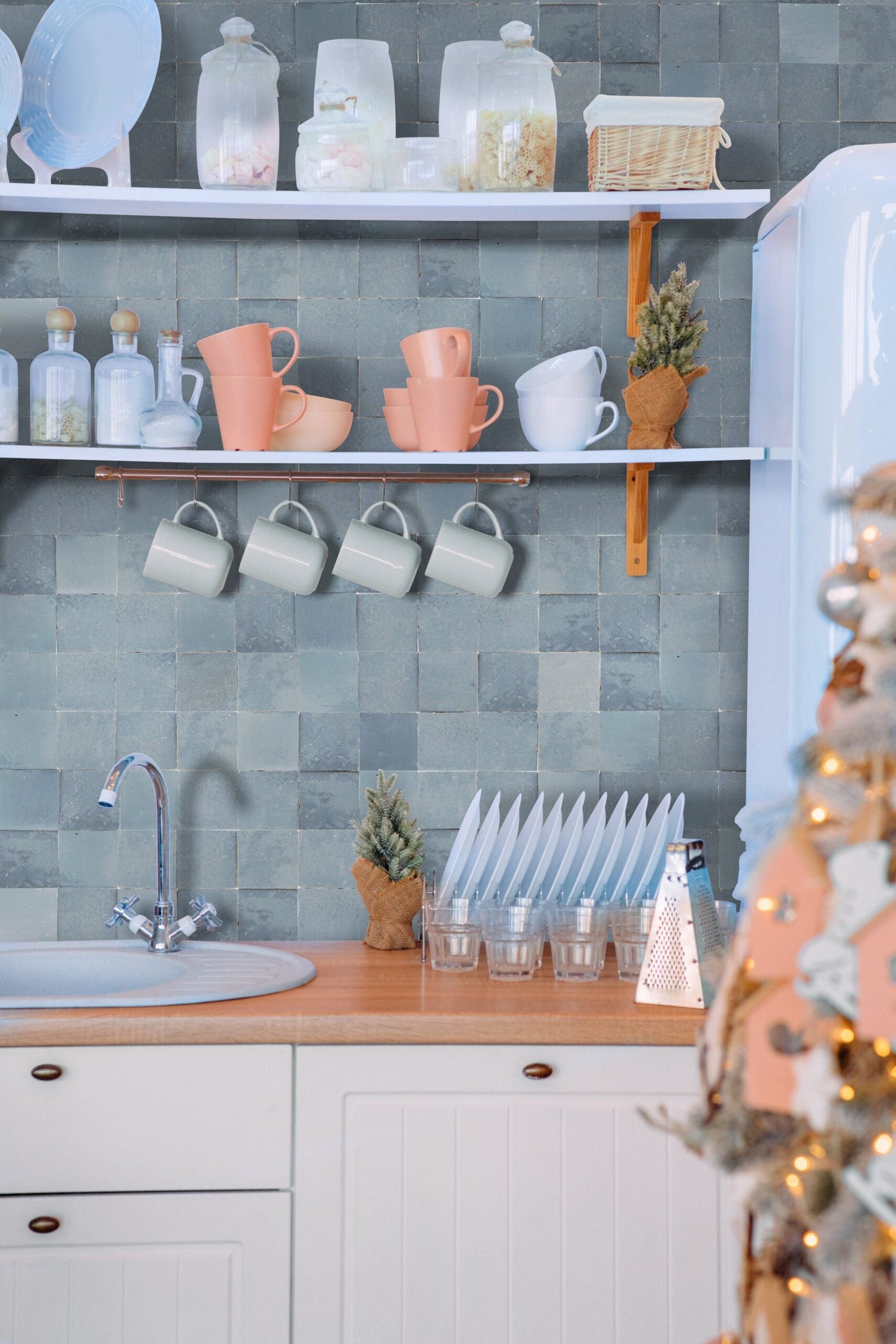 Ash Grey tiles by New York Cement Tile and pastel kitchenware on shelves above the sink add charm to the space.