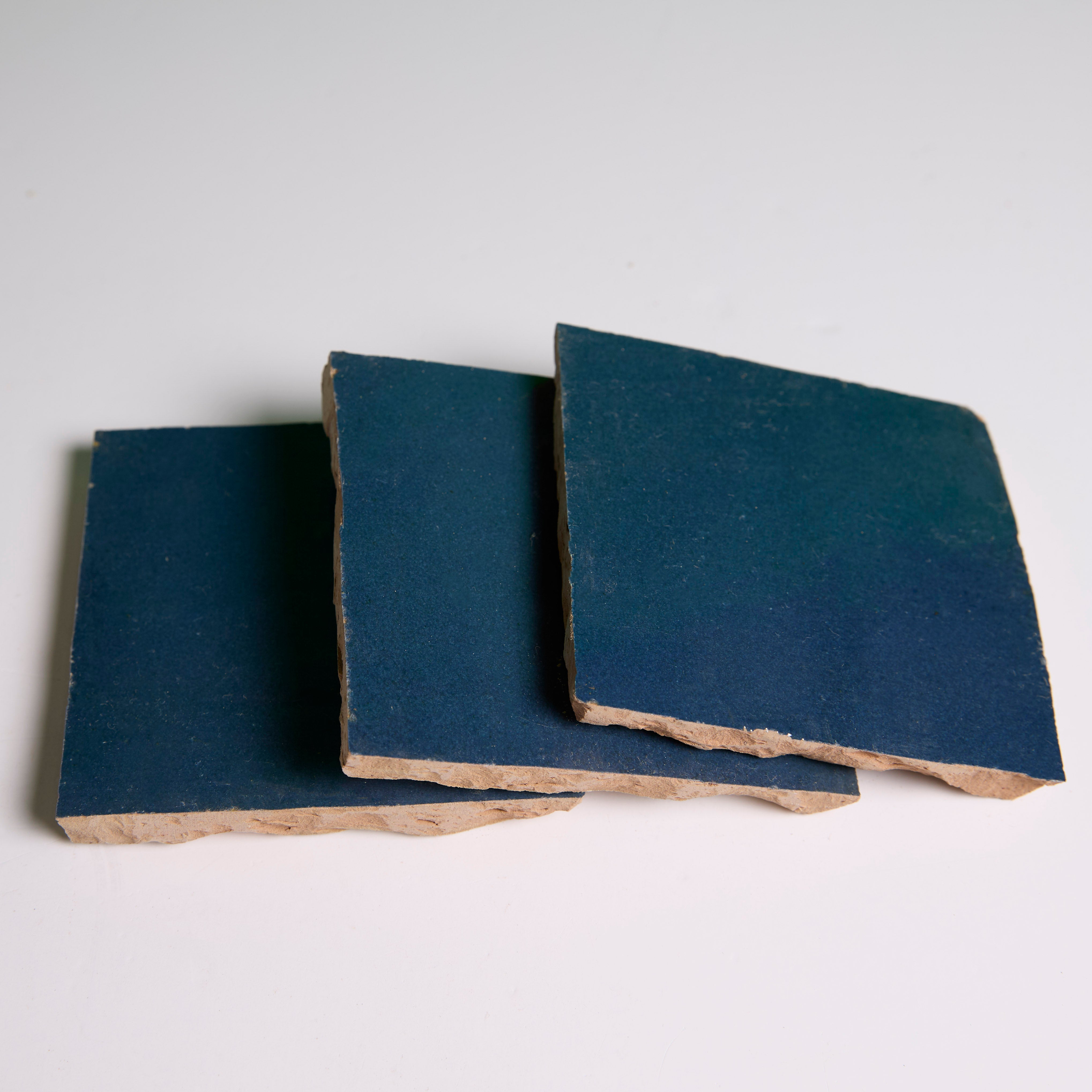 Three Sea Breeze tiles by New York Cement Tile with rough edges stacked on a white surface.