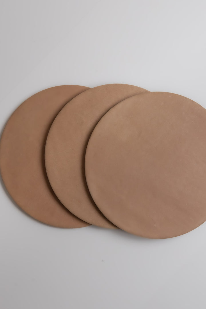 Three round, flat Arcilla samples by Finca, in light brown, overlap on a white surface.