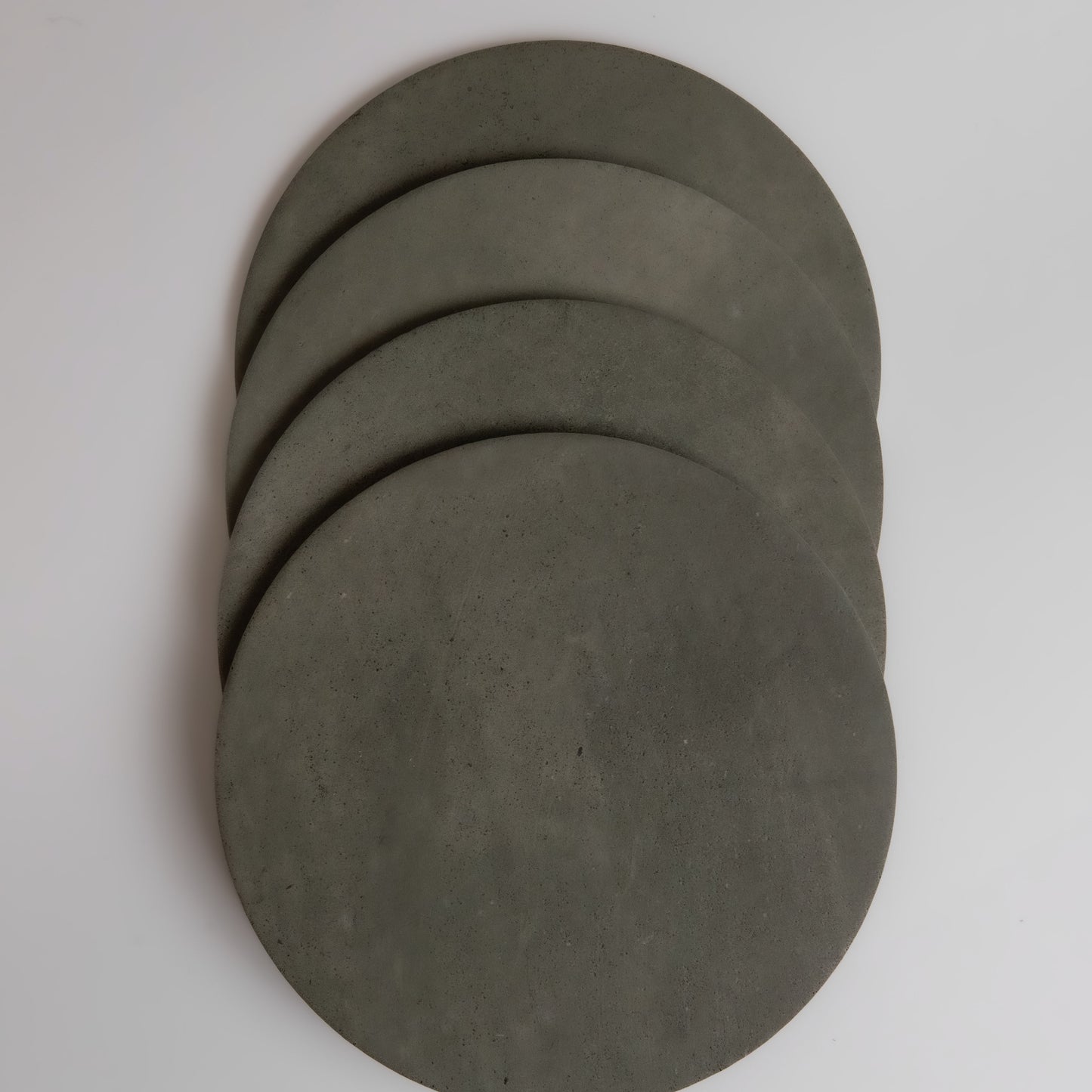Four round, flat, gray Finca Cardon Extra Sample concrete discs overlap on a white background.