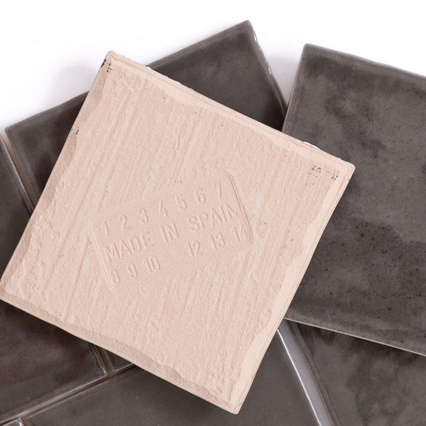 A Cobbled Graphite tile by Cottage Ivy rests atop several glossy dark gray tiles.
