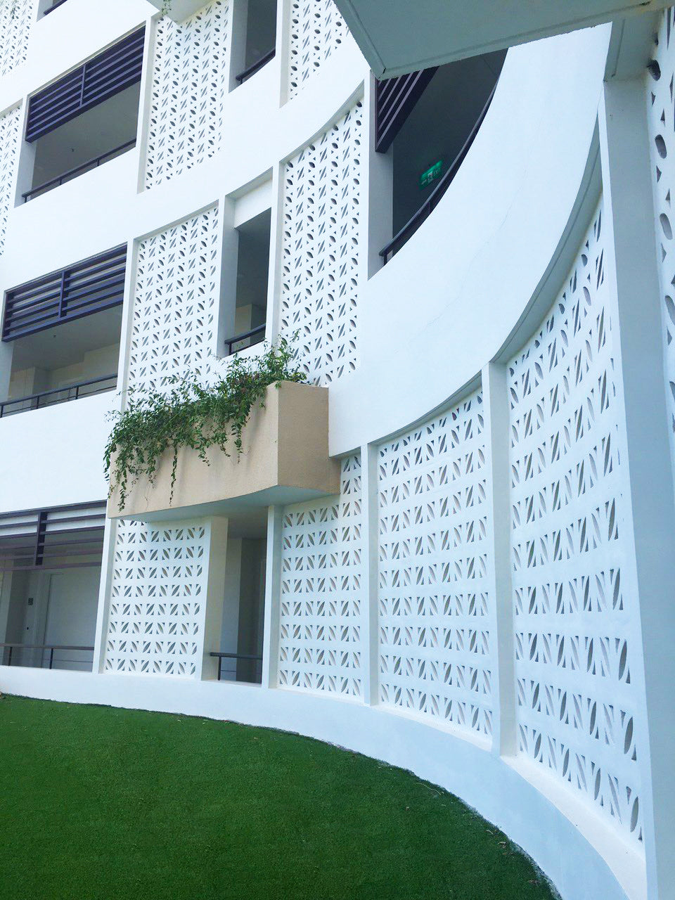 Curved white Coz breeze blocks by New York Cement Tile, tan planter with vines, and artificial grass below.