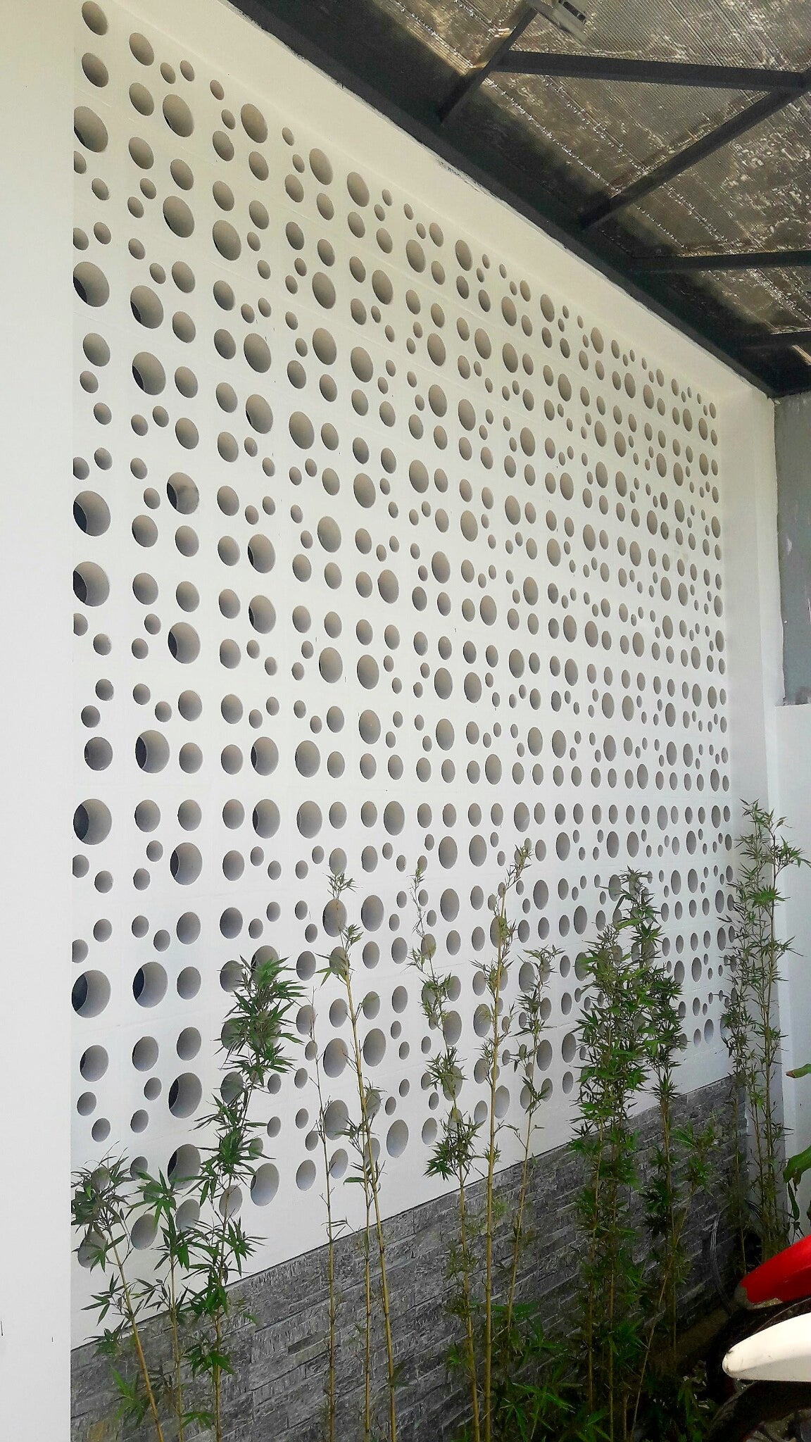 The Jami wall panel by New York Cement Tile features circular holes, bamboo accents, and a stone base.