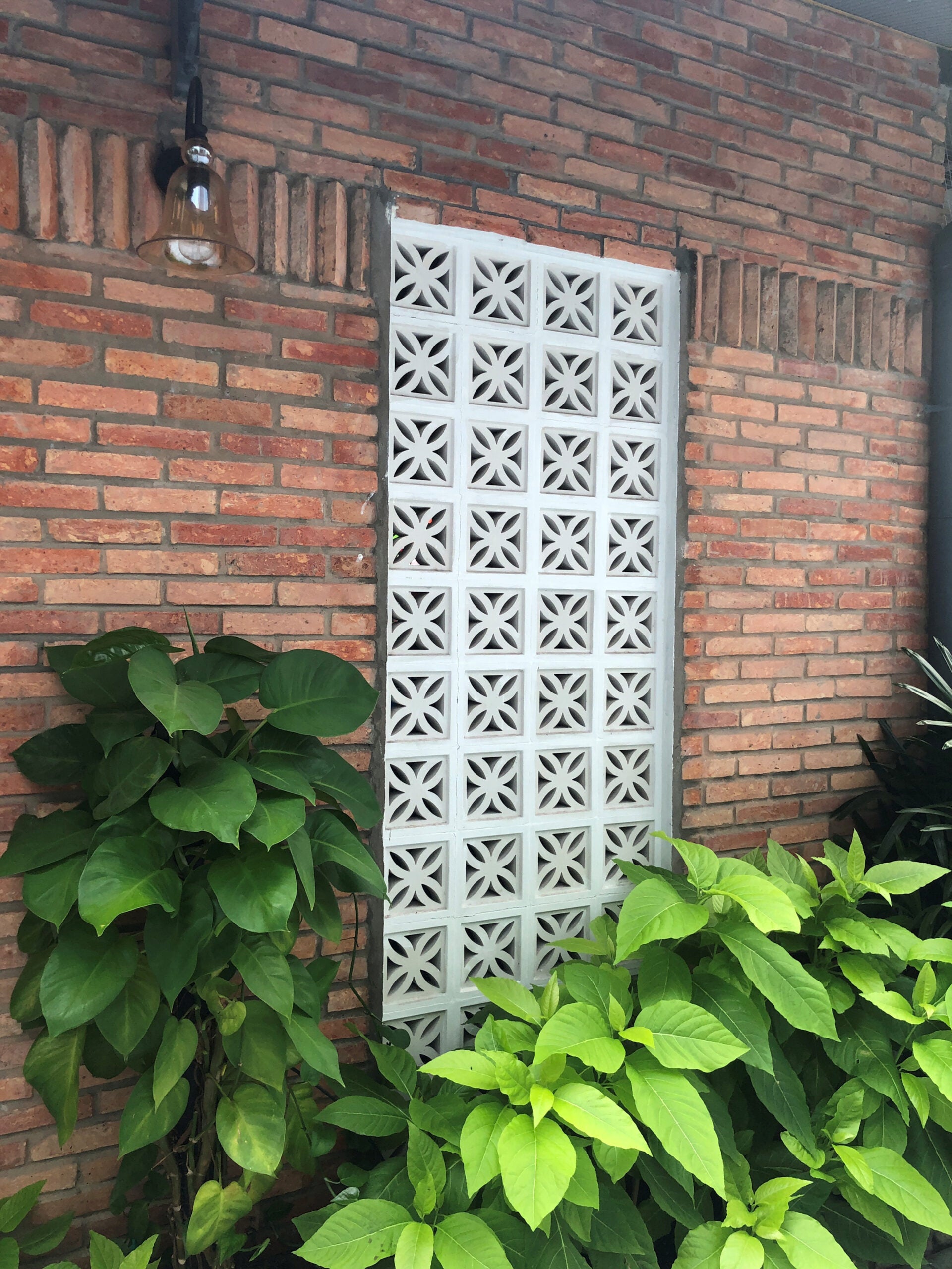 Beeza Sample by New York Cement Tile: white rectangular breeze blocks accent a red brick wall with green leafy plants.