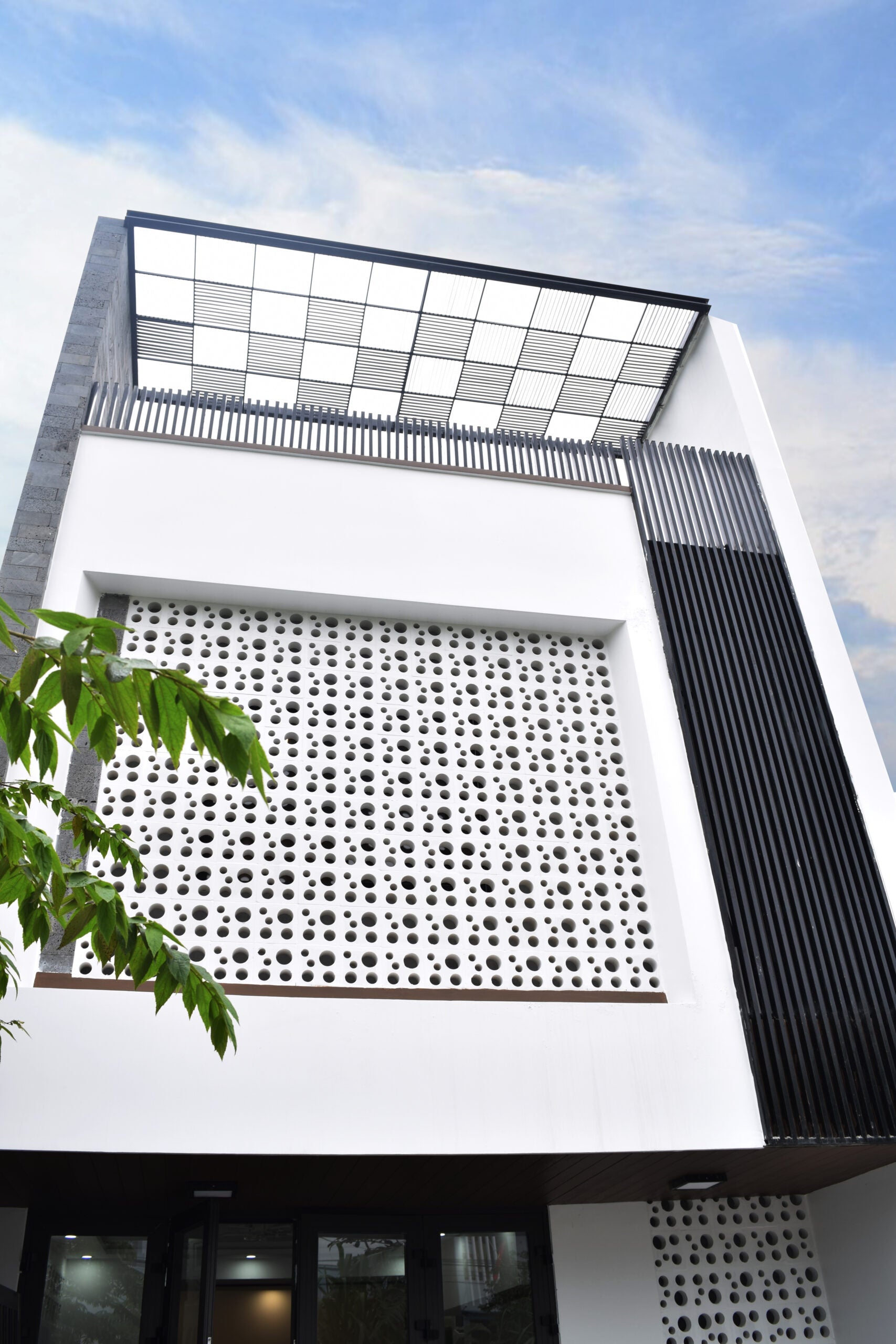 Jami by New York Cement Tile: Modern white building with breeze blocks, black slats & grid rooftop under a blue sky.