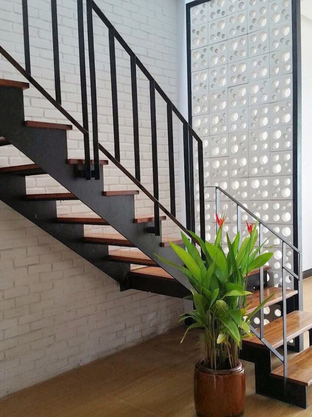 Jami by New York Cement Tile: Modern staircase with black railing, wood steps, potted plant & white breeze block wall.