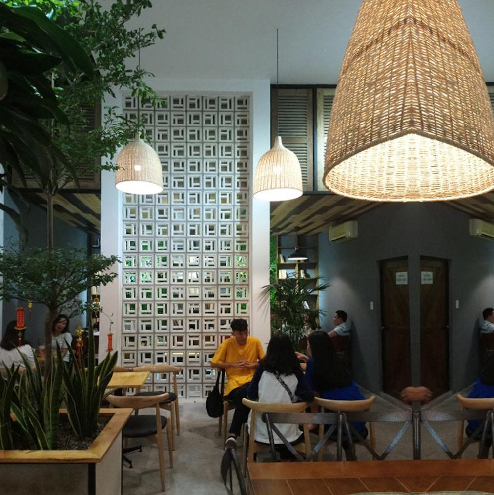 People sit and talk at wooden tables in a cafe featuring Katai Sample tiles by New York Cement Tile, woven lamps, and plants.
