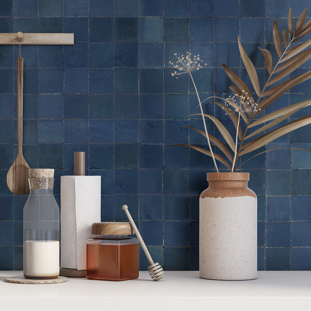 Ceramic vase, dried plants, honey jar, and utensils on a white counter with Navy Depths tiles by New York Cement Tile.