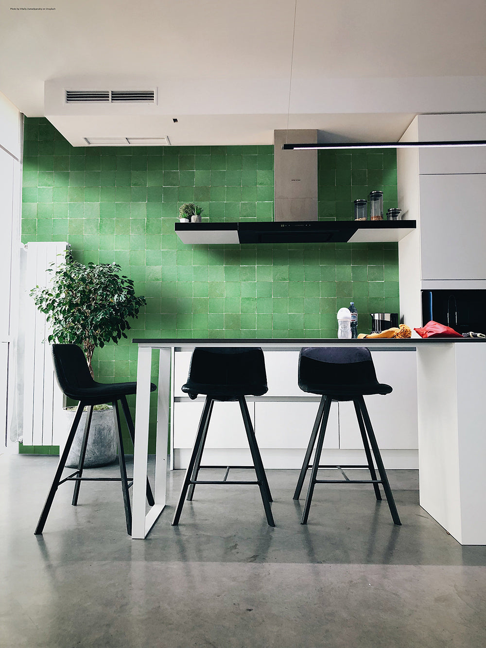 Modern kitchen featuring a Forest Green 2X2 backsplash by New York Cement Tile, three black bar stools, and a white island.