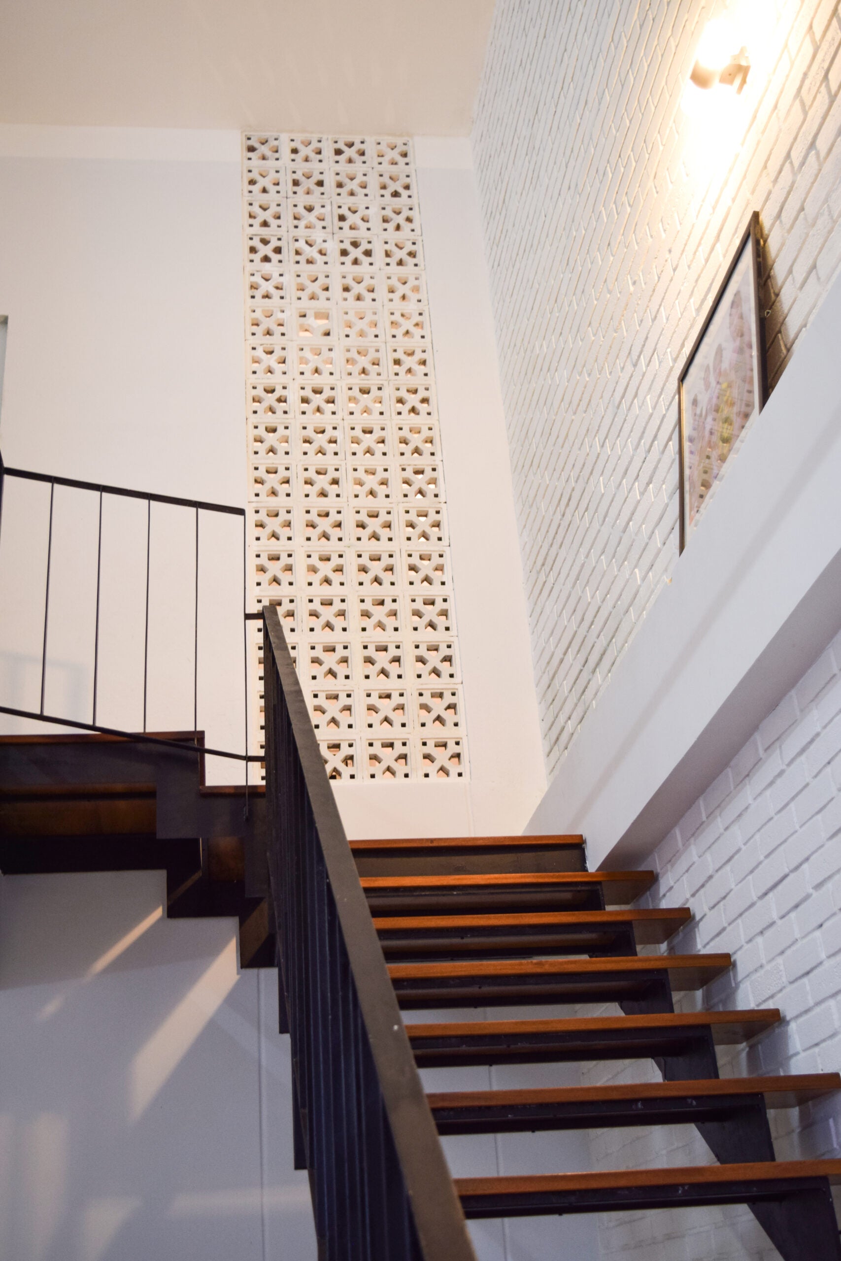 The Tahit by New York Cement Tile features wooden steps, black railings, and a white brick wall with breeze blocks.