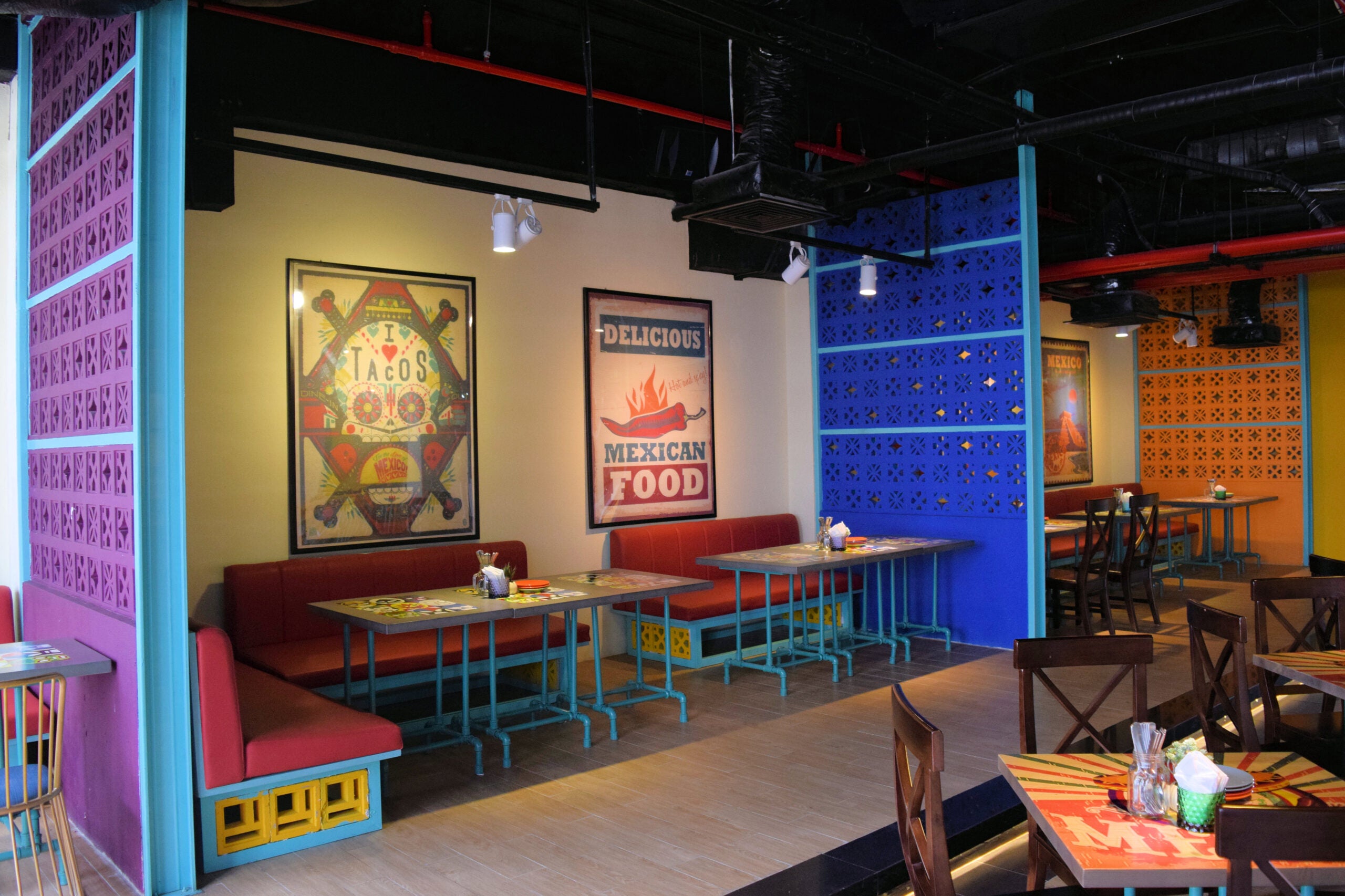 Sam by New York Cement Tile features colorful wall art, blue partitions, red benches, and wooden tables and chairs.