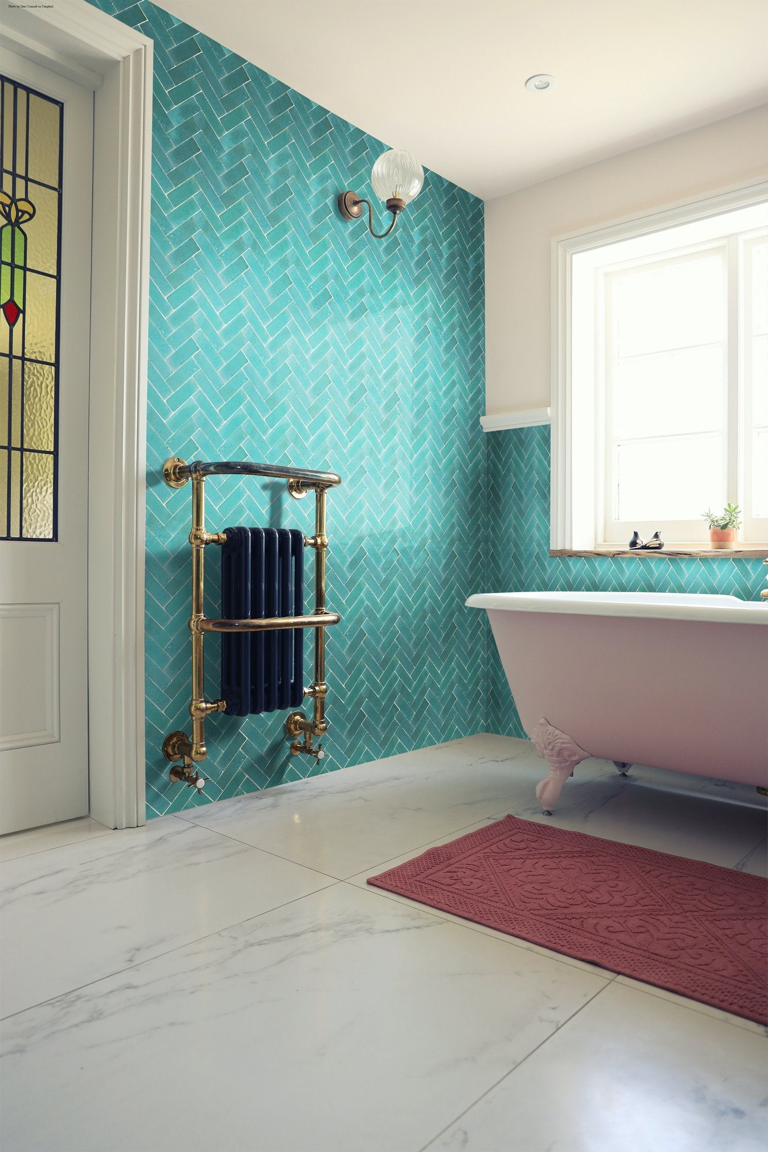 A bathroom with Seafoam (2x6) tile walls by New York Cement Tile, a white tub, brass radiator, and red mat on white floor.