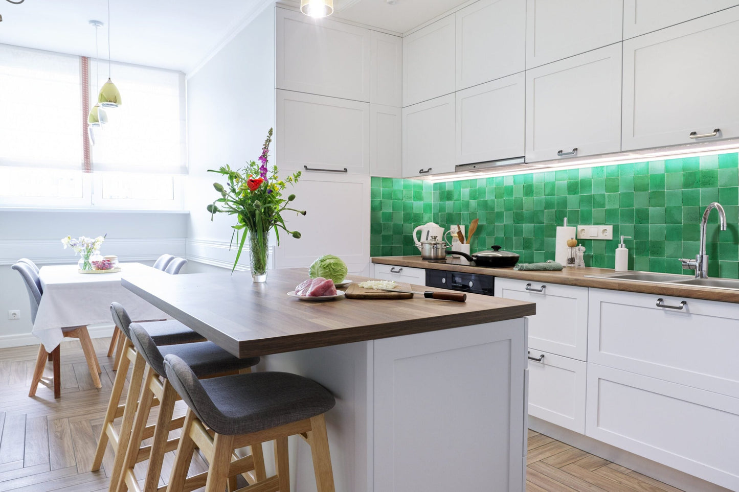 Modern kitchen with Jewel Green zellige tile by New York Cement Tile, white cabinets, wood island, and counter flowers.