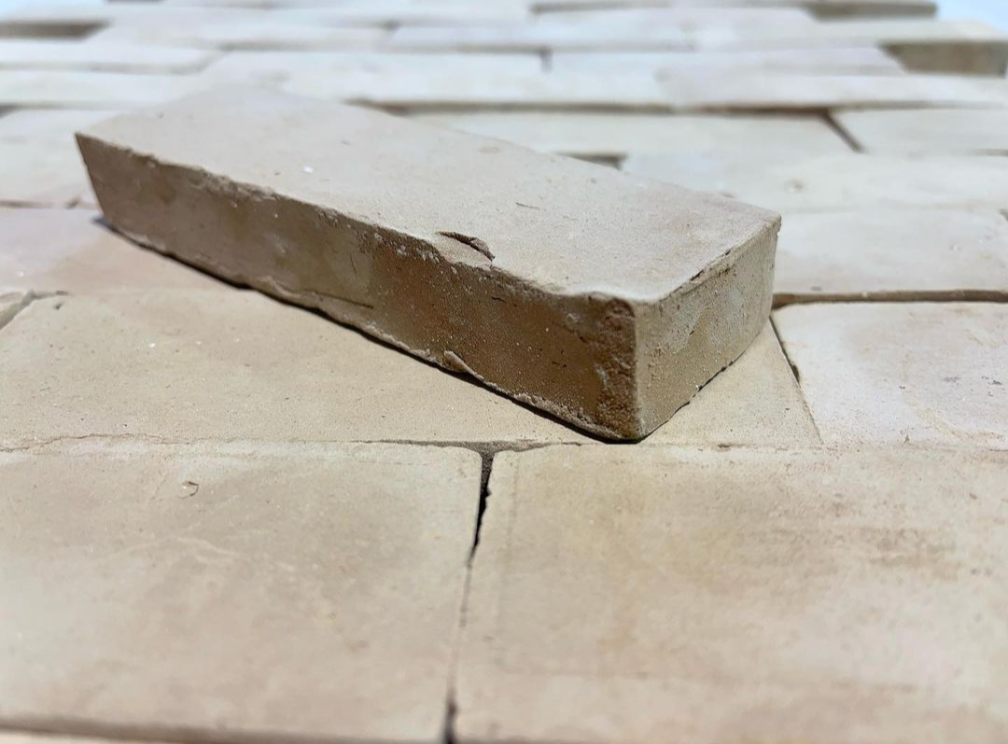 A single light brown brick resting on top of a surface made of similar flat bricks.