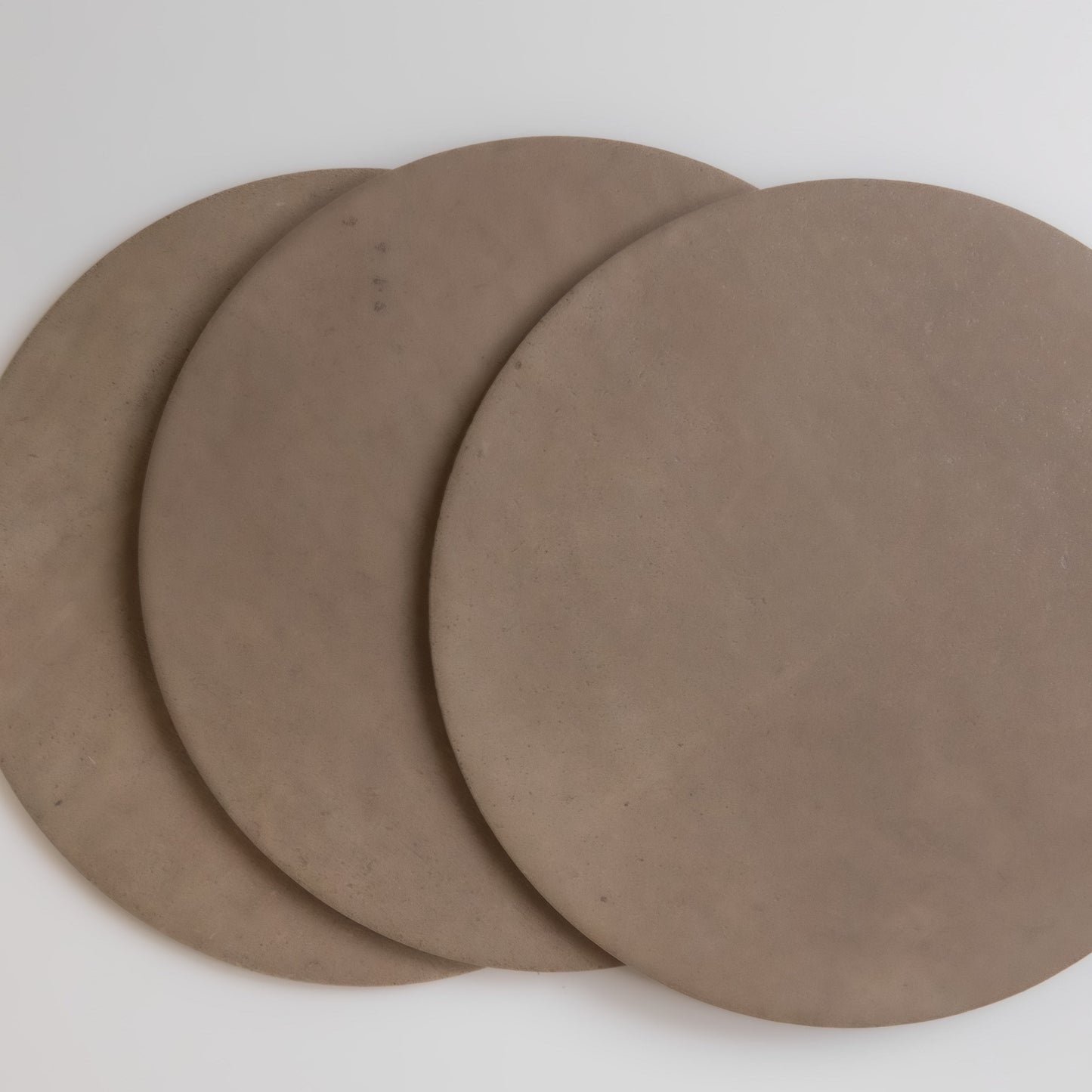 Three overlapping round brown Pampas clay slabs by Finca on a white surface, viewed from above.