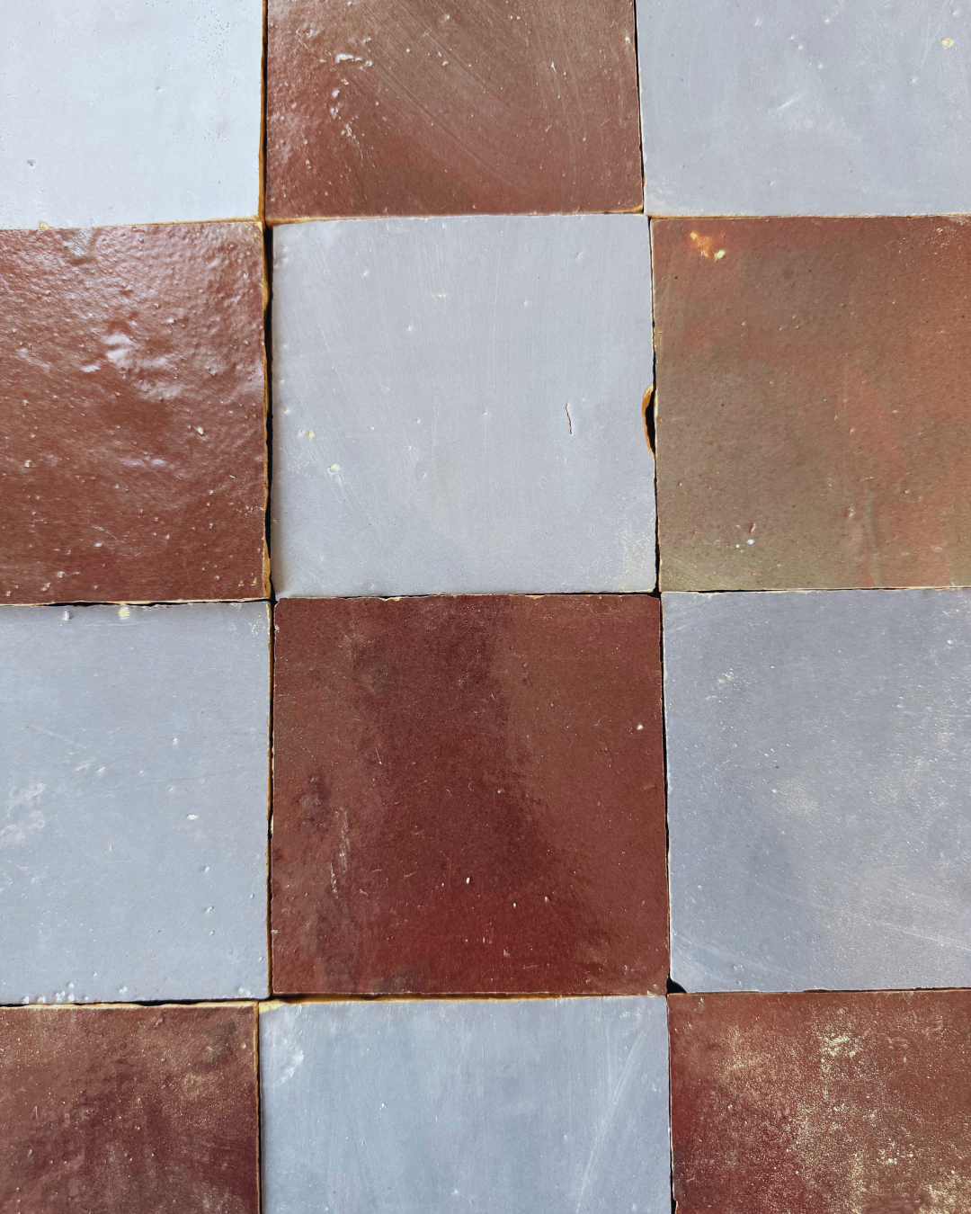 Steel Grey handcrafted tiles by New York Cement Tile feature a checkerboard of reddish-brown and gray with visible seams and texture.