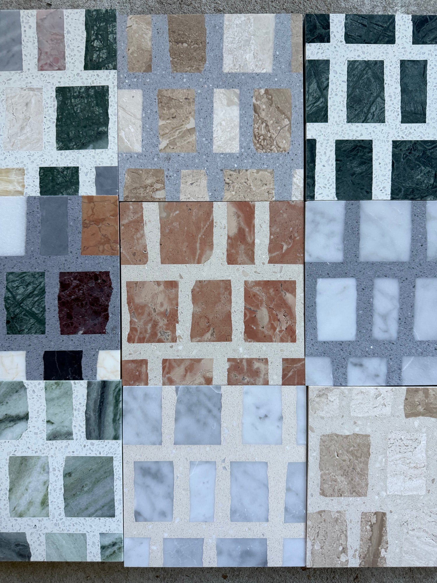 Nine rectangular tiles with grid patterns made of various colored stone squares, including green, brown, red, gray, white, beige, and marble, arranged together on a flat surface.