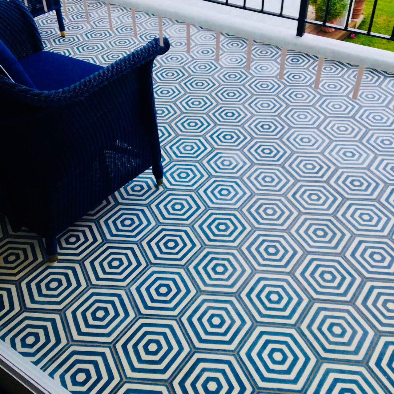 A blue chair on a patio with a blue and white hexagonal geometric tile floor, seen through glass.
