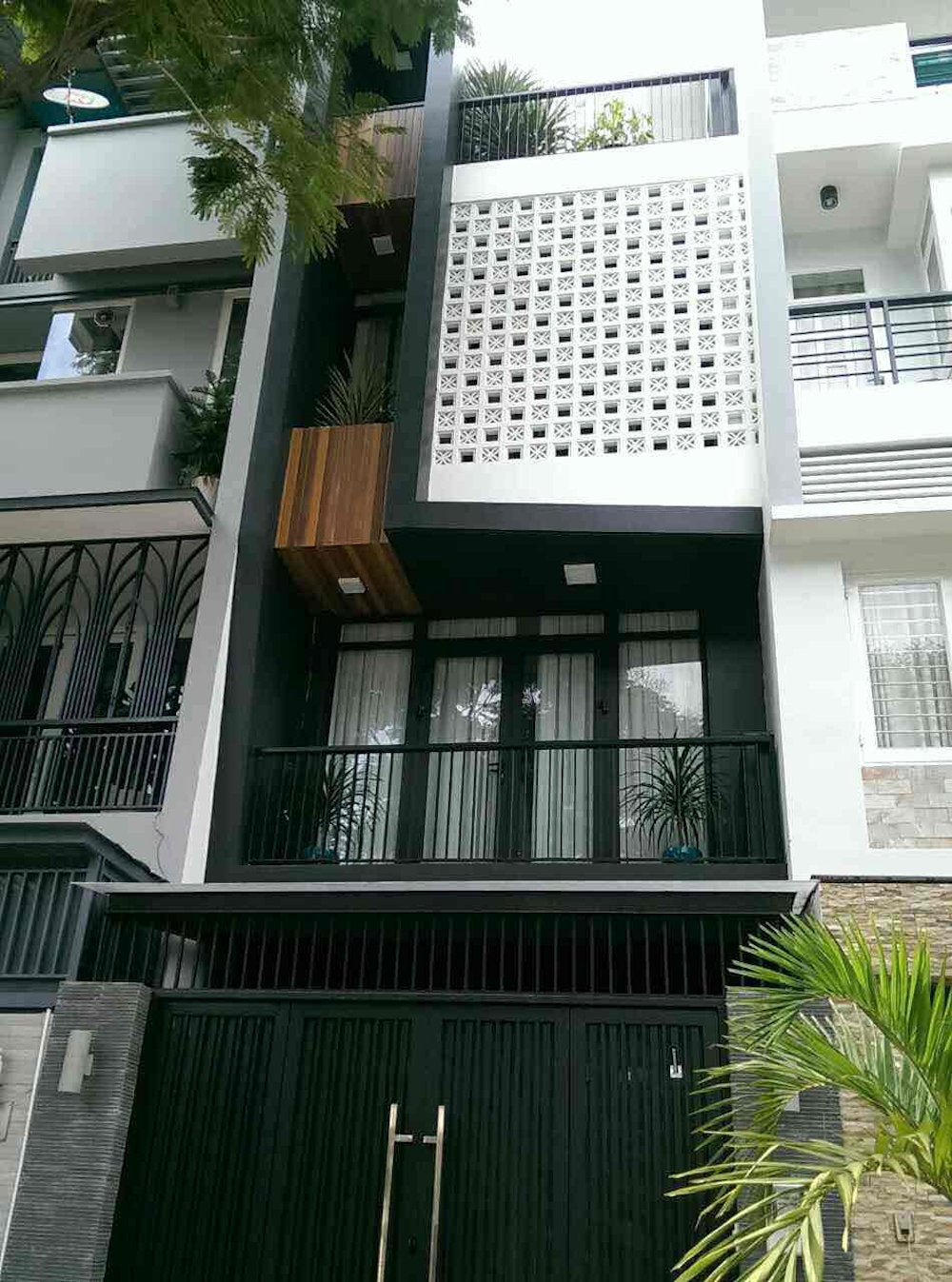 Modern three-story house with a black gate, balcony, and Beeza Sample breeze blocks by New York Cement Tile on the upper floor.