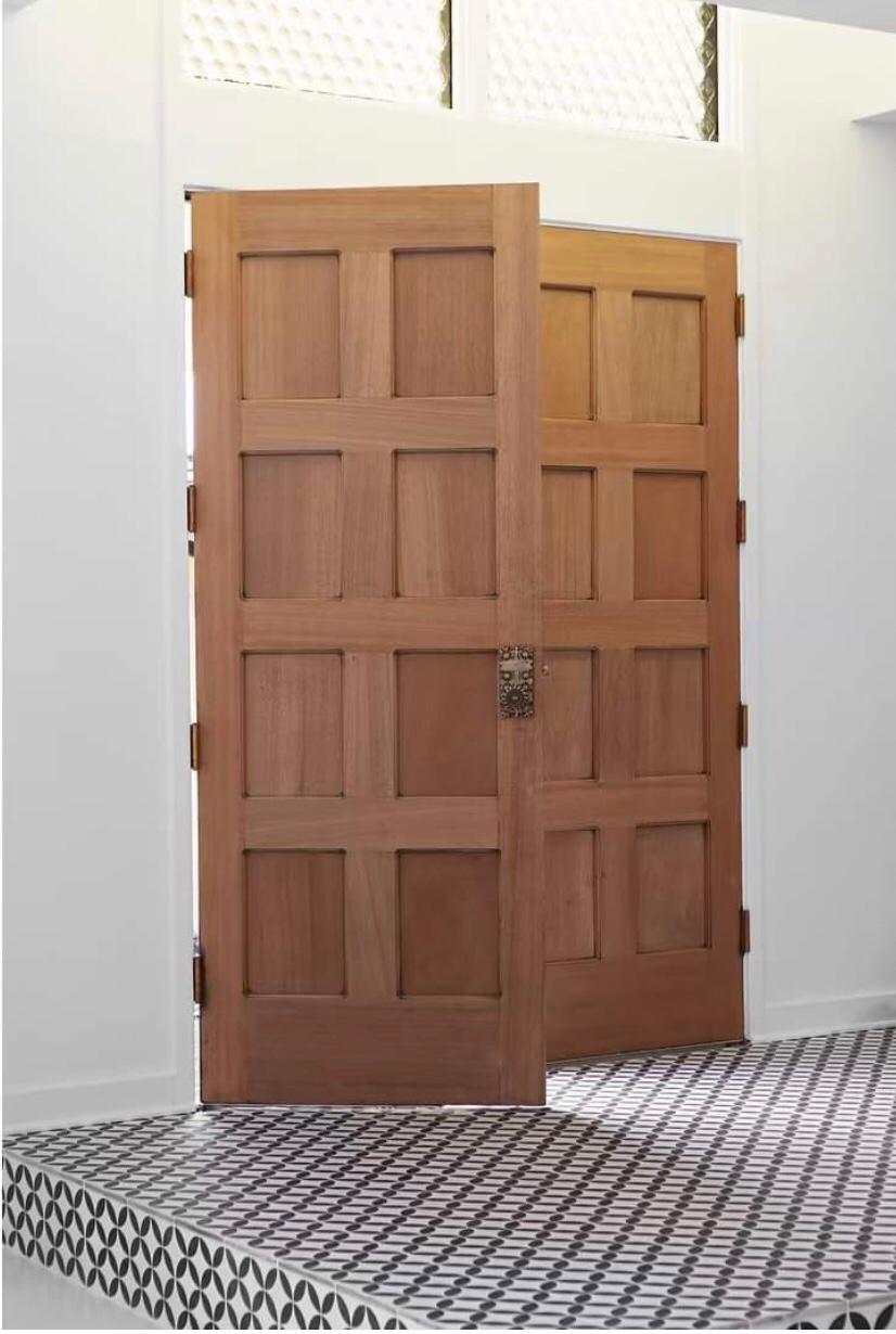A wooden double door, partially open, on patterned tile flooring with white walls and glass panels above.