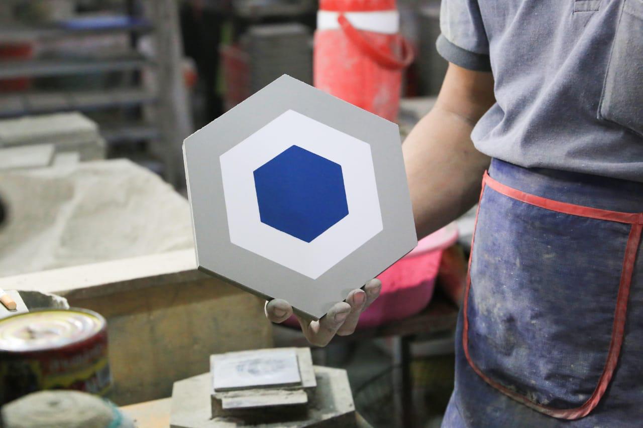 A person holds a hexagonal tile with a blue hexagon in the center and gray and white borders.