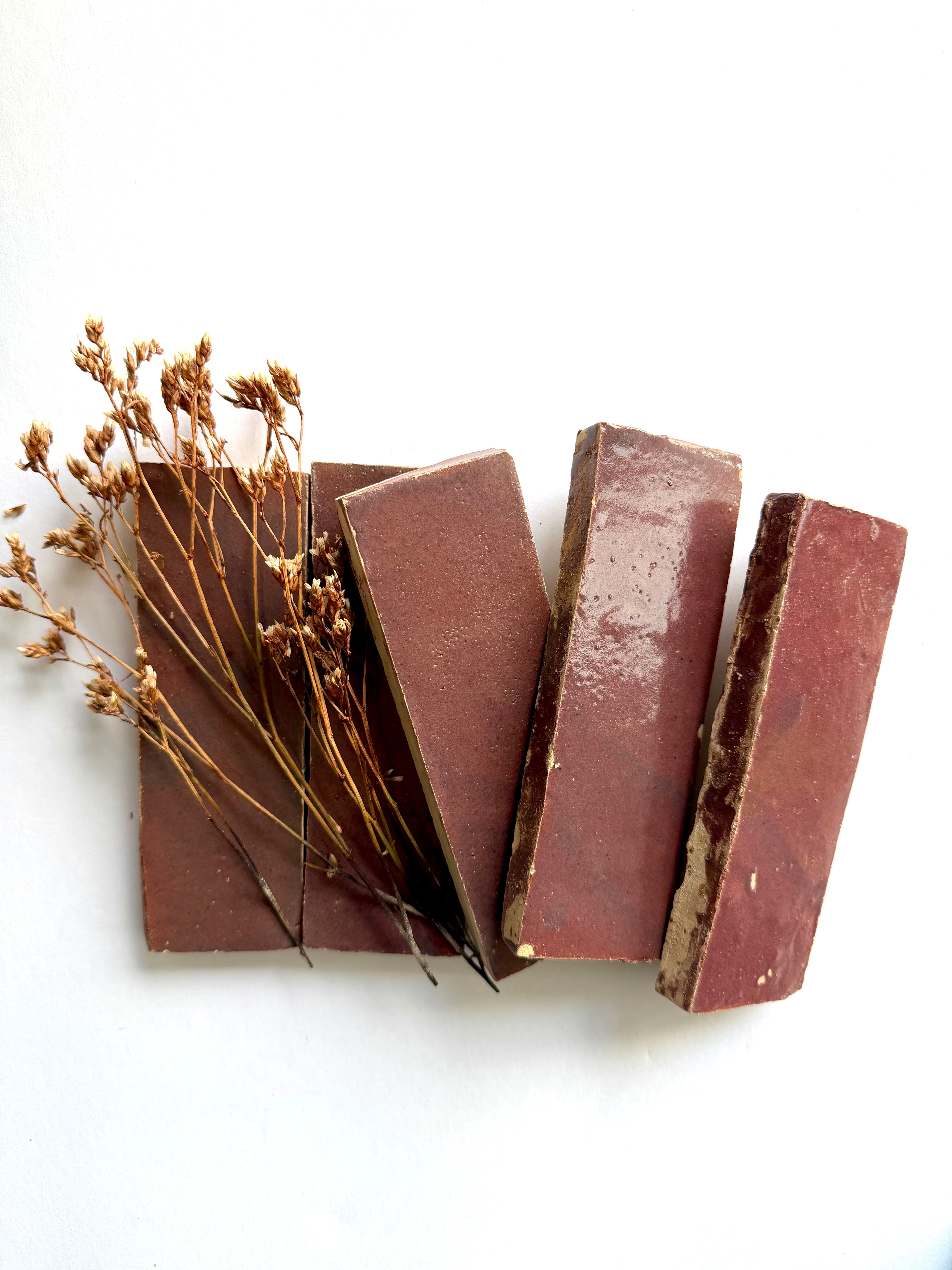 Four Thistle (2x6) tiles by New York Cement Tile arranged diagonally with brown soap bars and dried flowers.