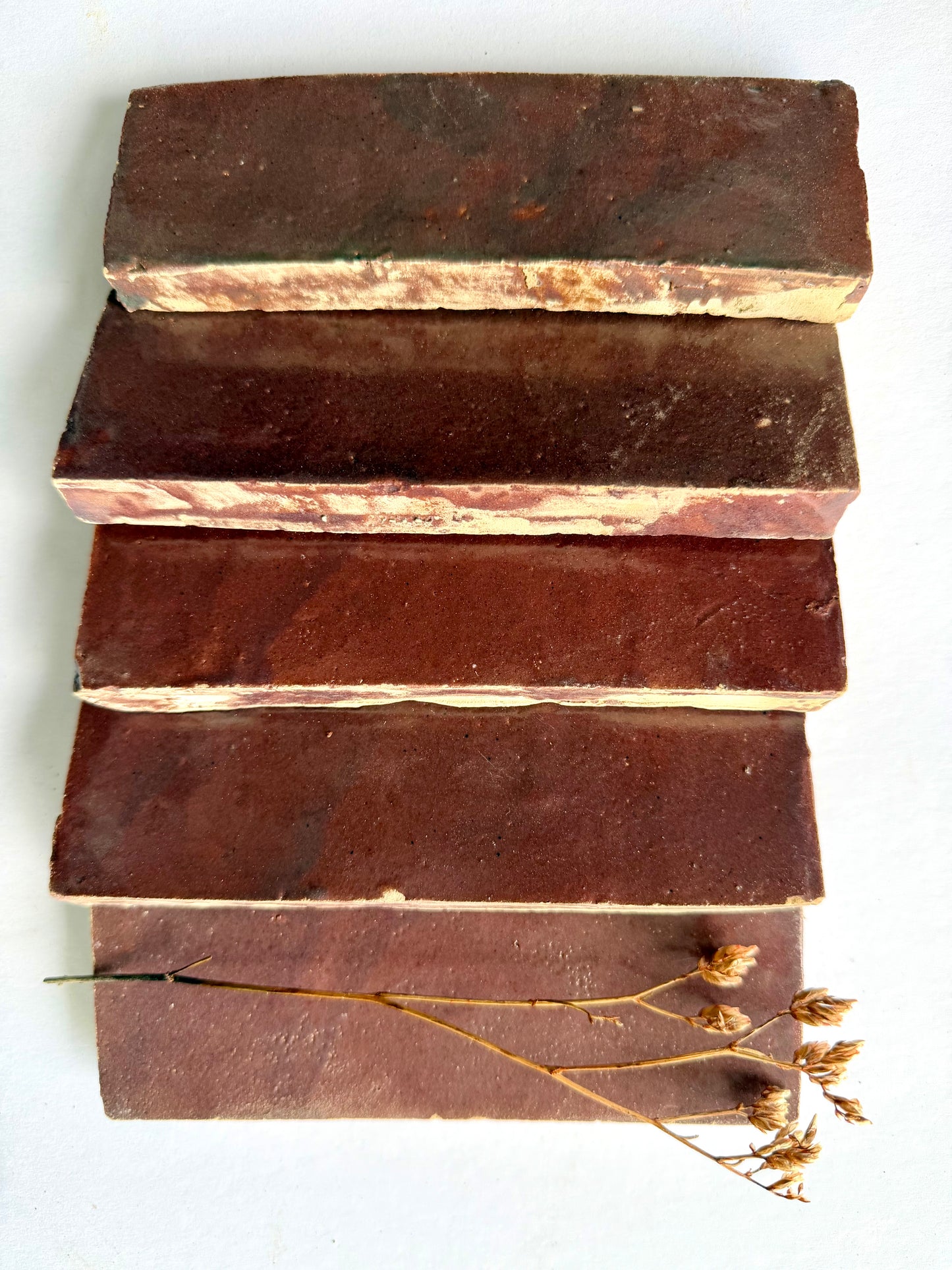 Five Thistle (2x6) brown bars by New York Cement Tile, stacked horizontally with a dried flower on white background.