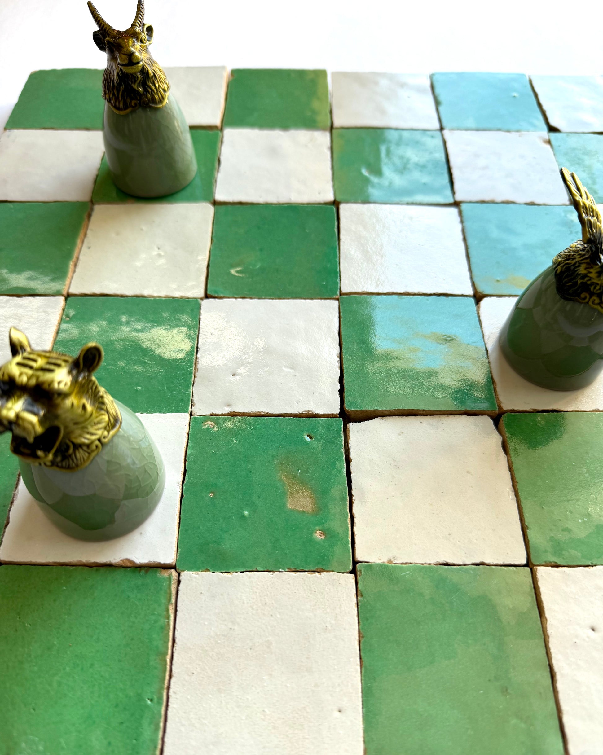 Three ornate chess pieces on a 2X2 Checkerboard Zellige in Ivory Cloud and Green by New York Cement Tile.
