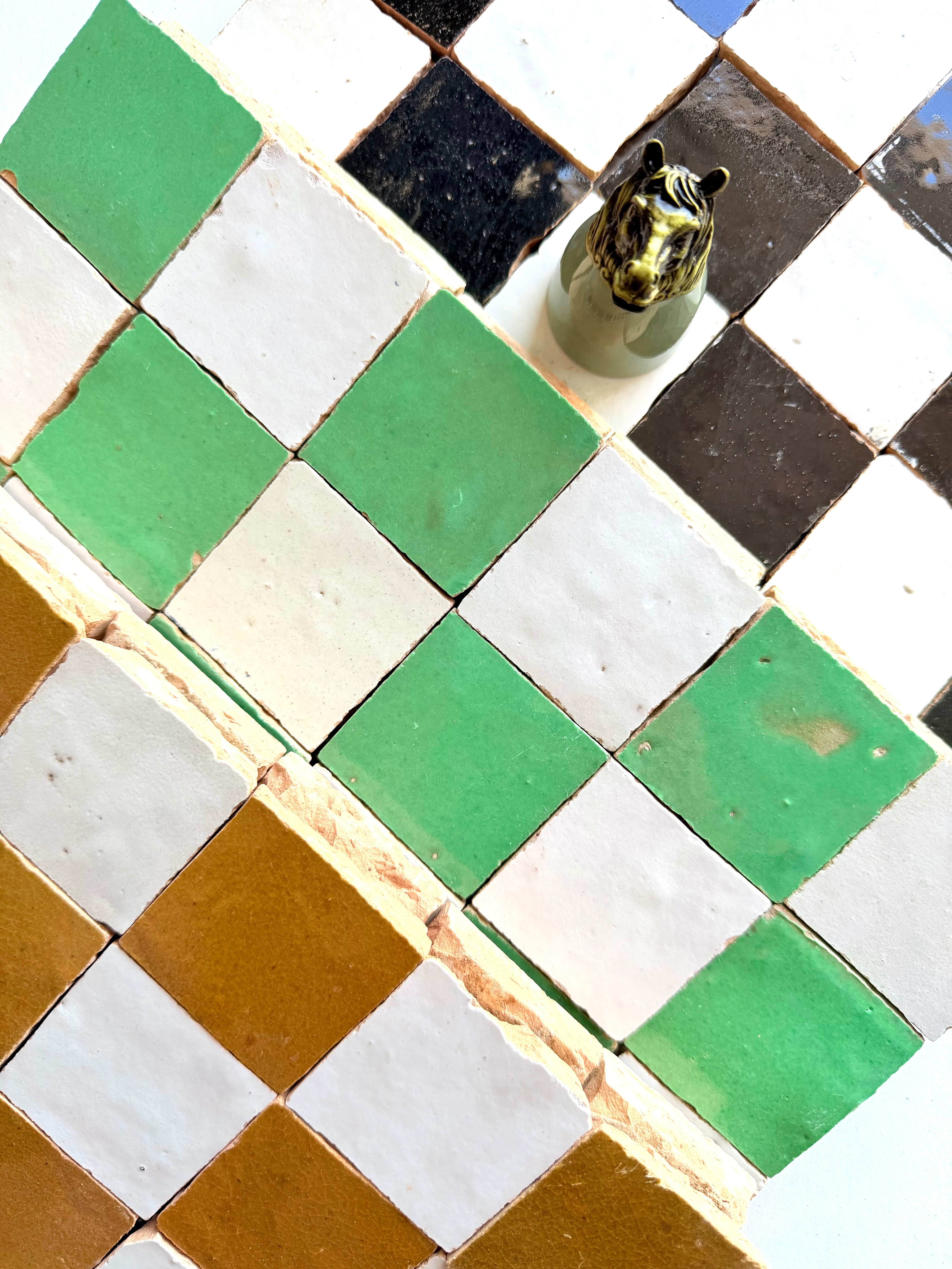 Checkerboard wall of 2X2 Checkerboard Zellige in Ivory Cloud and Green by New York Cement Tile, plus a small ceramic tiger head.