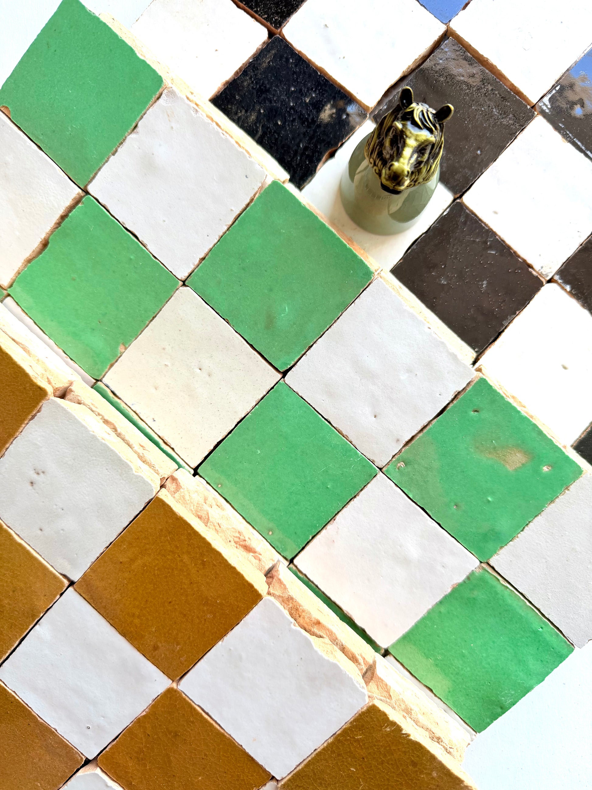 2X2 Checkerboard Zellige in Ivory Cloud & Caramel by New York Cement Tile lines the wall, with a small horse head sculpture.