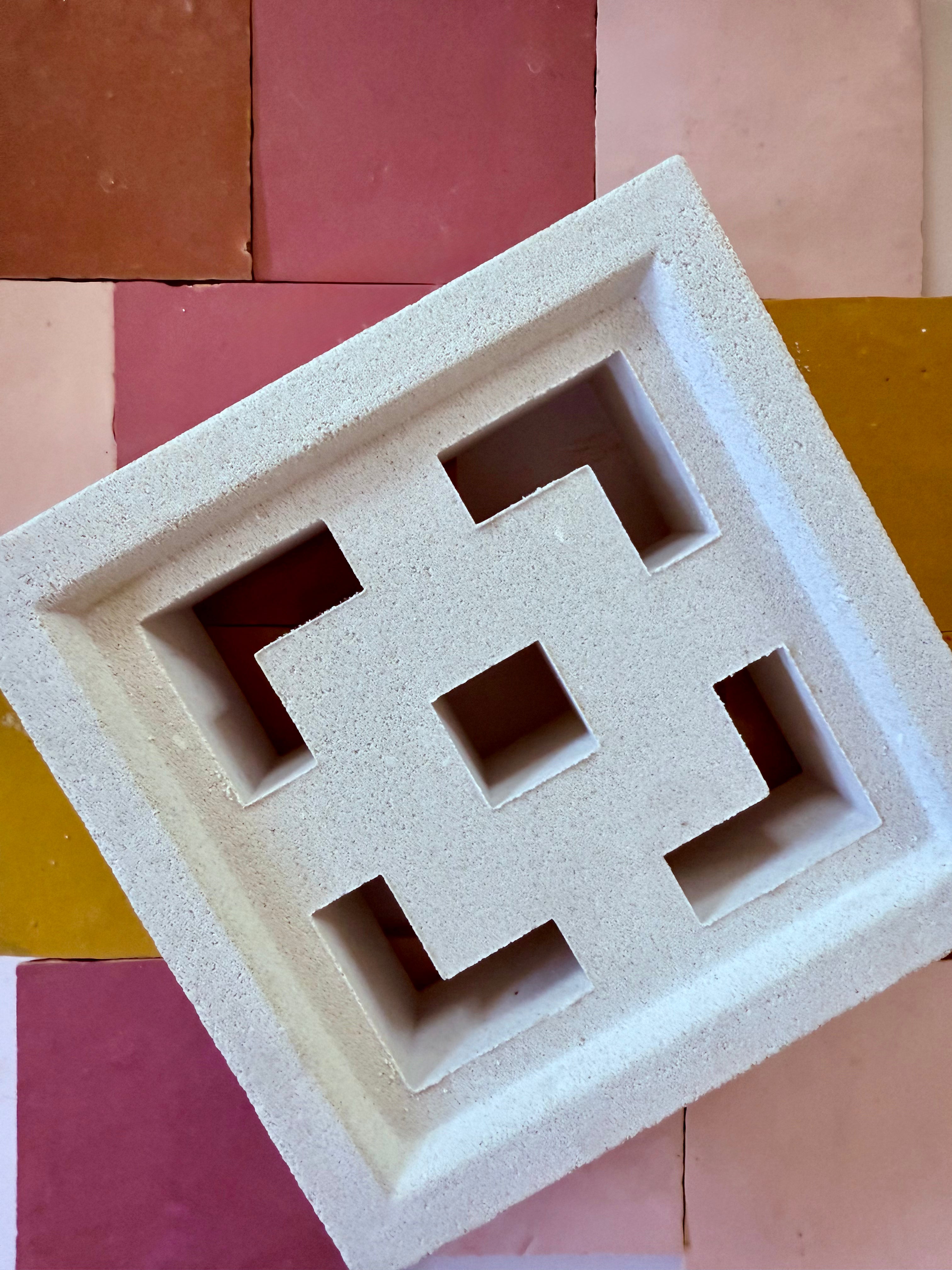 A white decorative concrete block with square cutouts sits on colorful pink and yellow tiles.