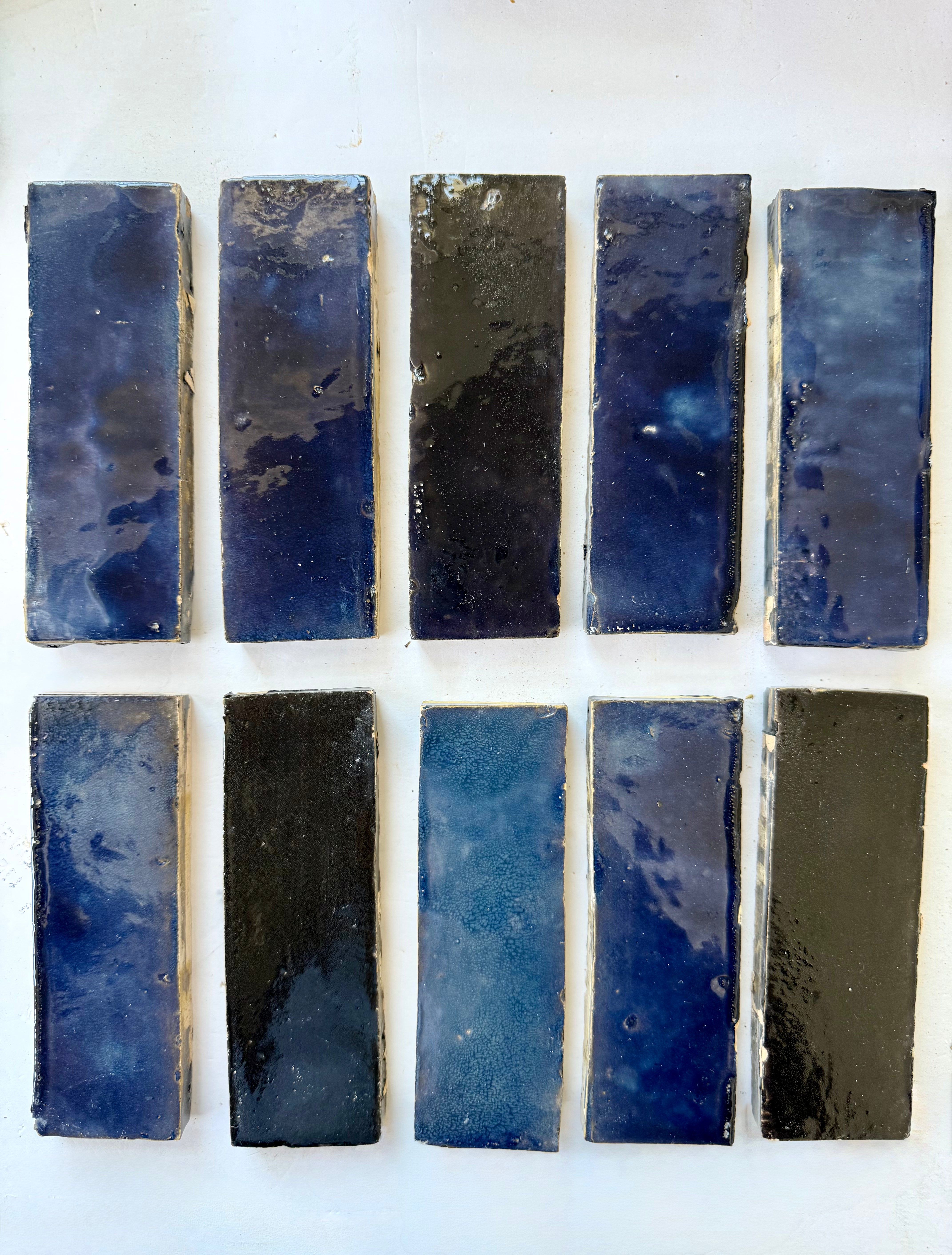 Ten Metallic Blue (2x6) tiles by New York Cement Tile, blue with black accents, are arranged in two rows on a white surface.