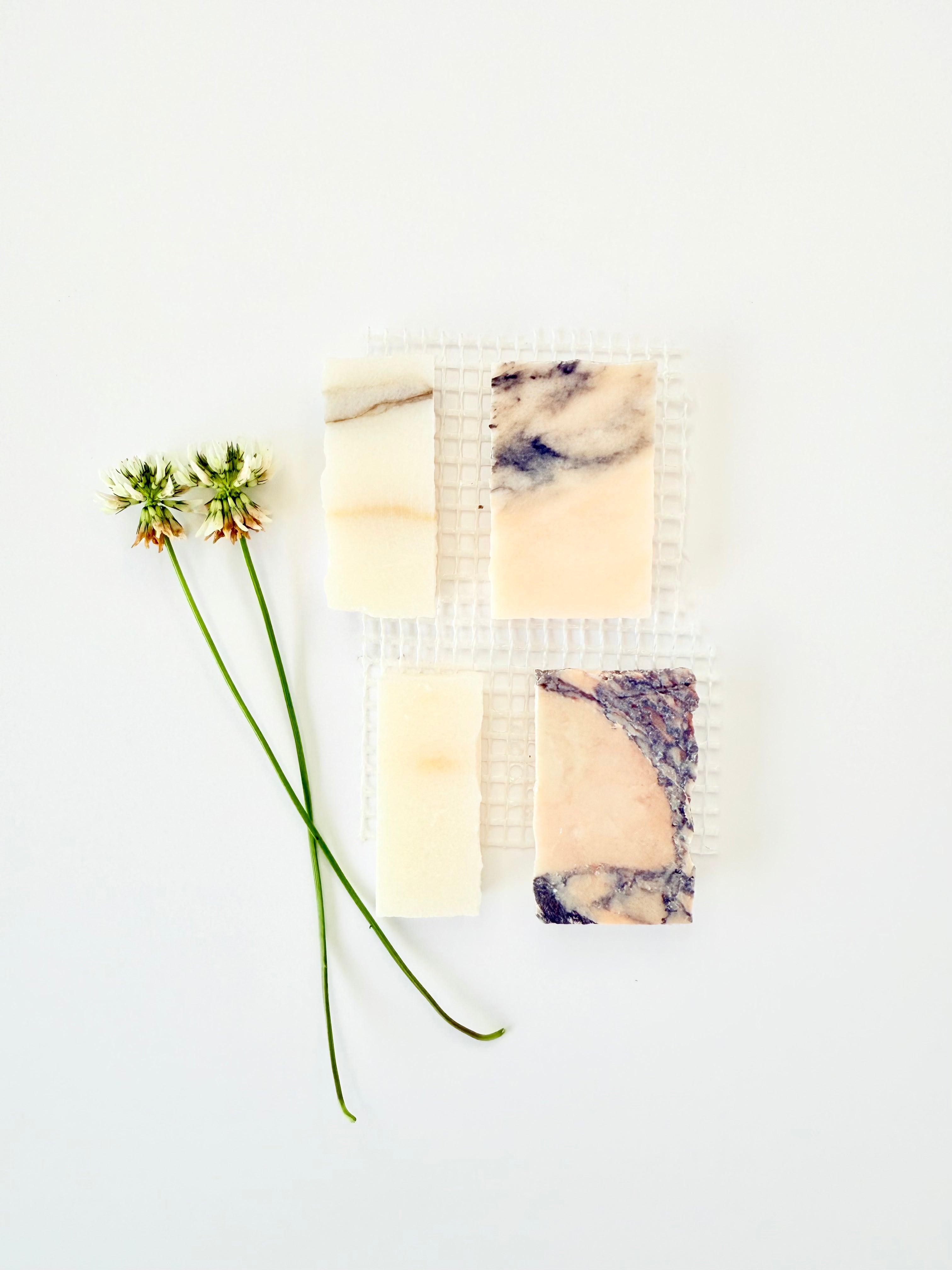 Four marbled soaps on New York Cement Tile's Scarpa I Mountain Mosaic Marble Mesh with white clover, against white background.