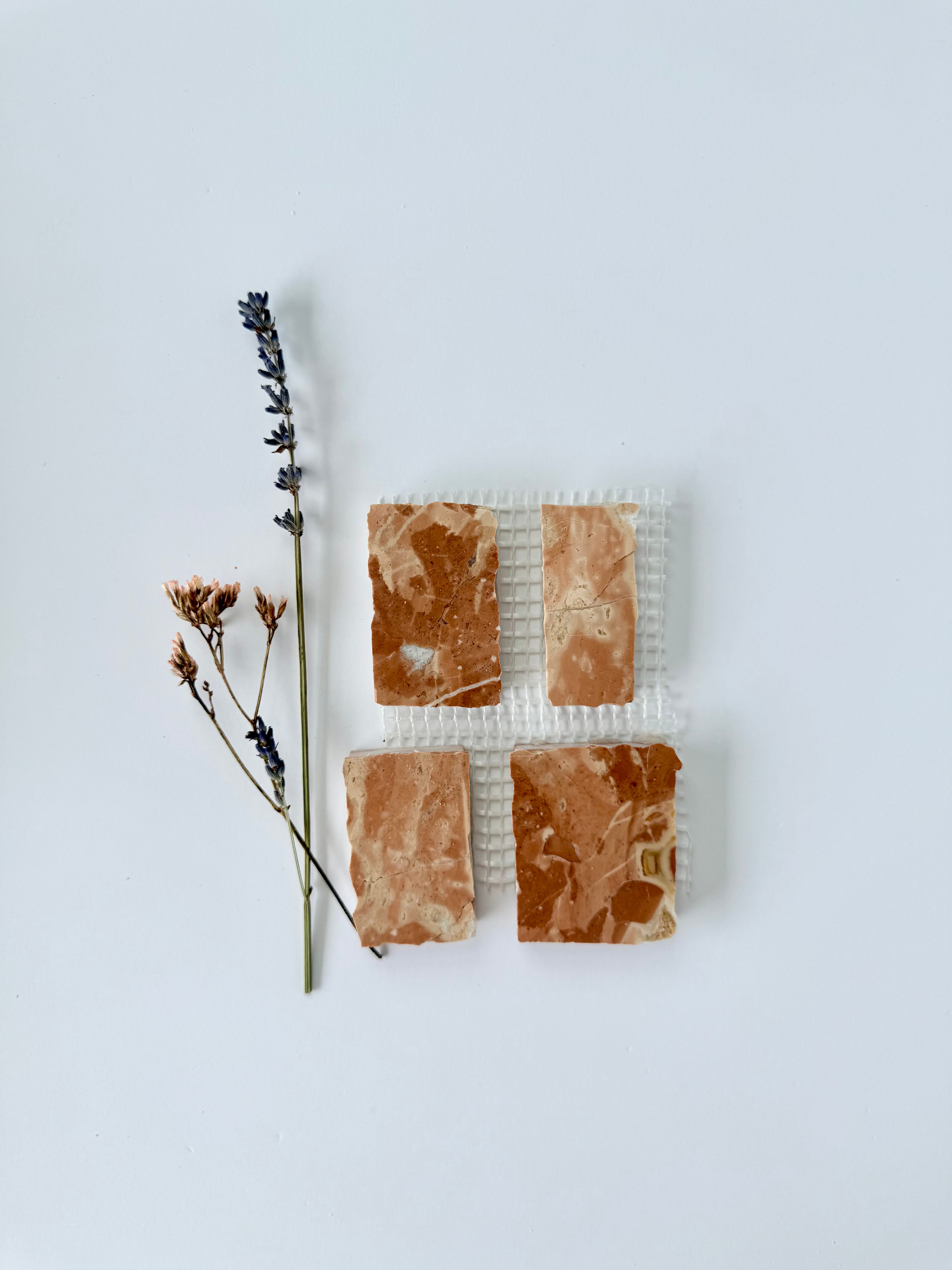 Four Scarpa I Earth Mosaic Marble Mesh tiles by New York Cement Tile with dried lavender on a white background.