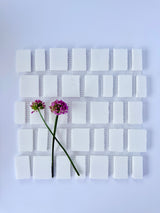 Two purple flowers rest on green stems atop New York Cement Tile’s Scarpa I Pure White Mosaic Marble Mesh.