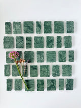 Scarpa I Emerald Mosaic Marble Mesh sample by New York Cement Tile, with green rectangular tiles in a grid and wildflowers on top.