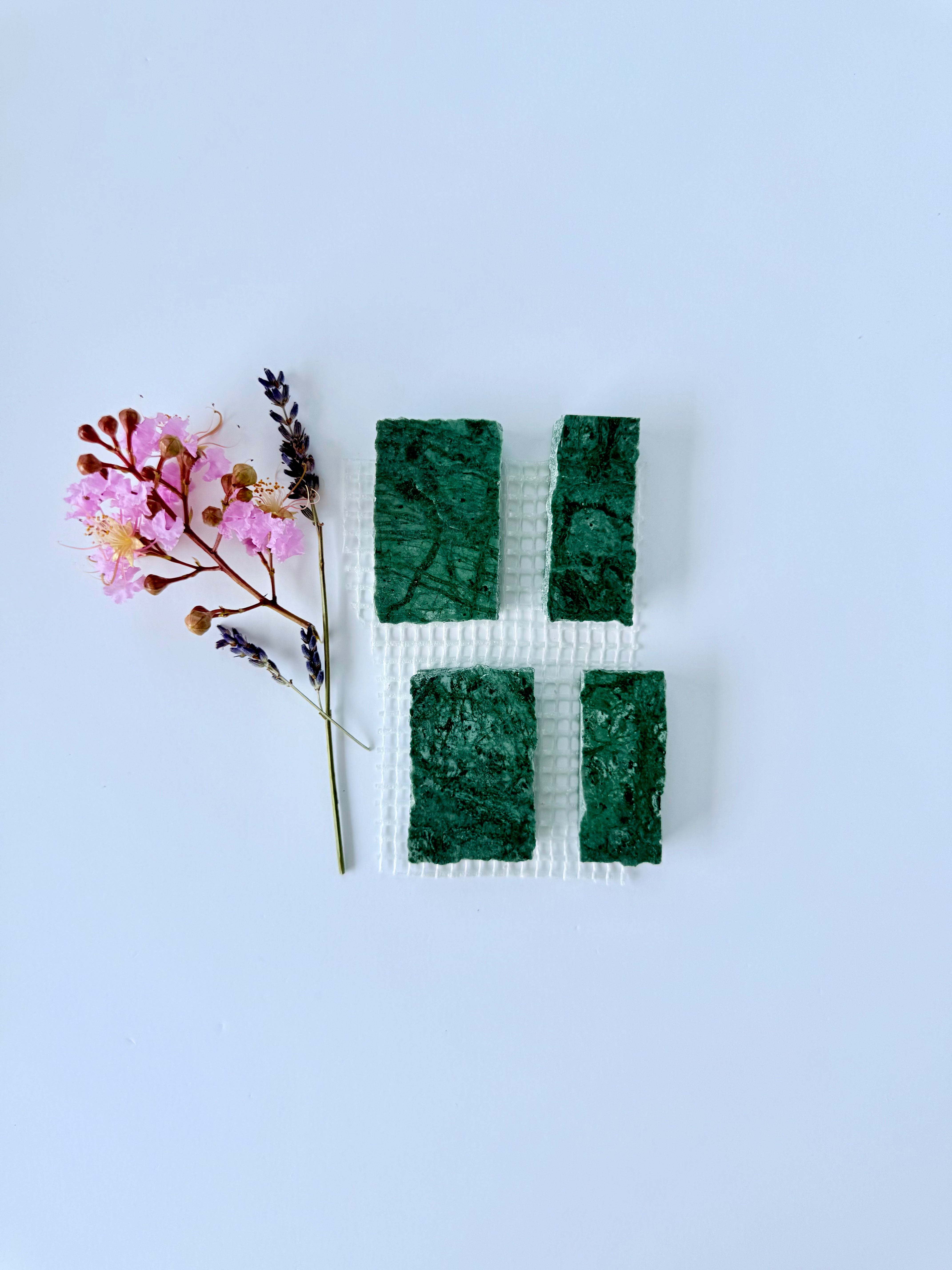 Four Scarpa I Emerald Mosaic Marble Mesh tiles by New York Cement Tile, shown with pink and purple flowers on white.